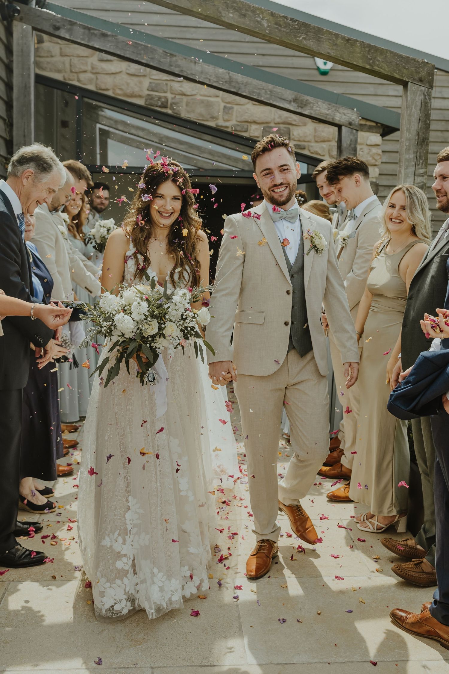 Wedding party celebrates on patio with flower petals falling through the air.