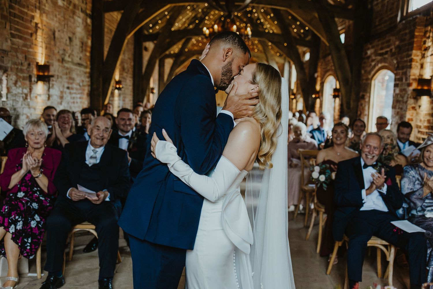 Wedding reception venue features elegant lighting and exposed brick walls with dancing guests.