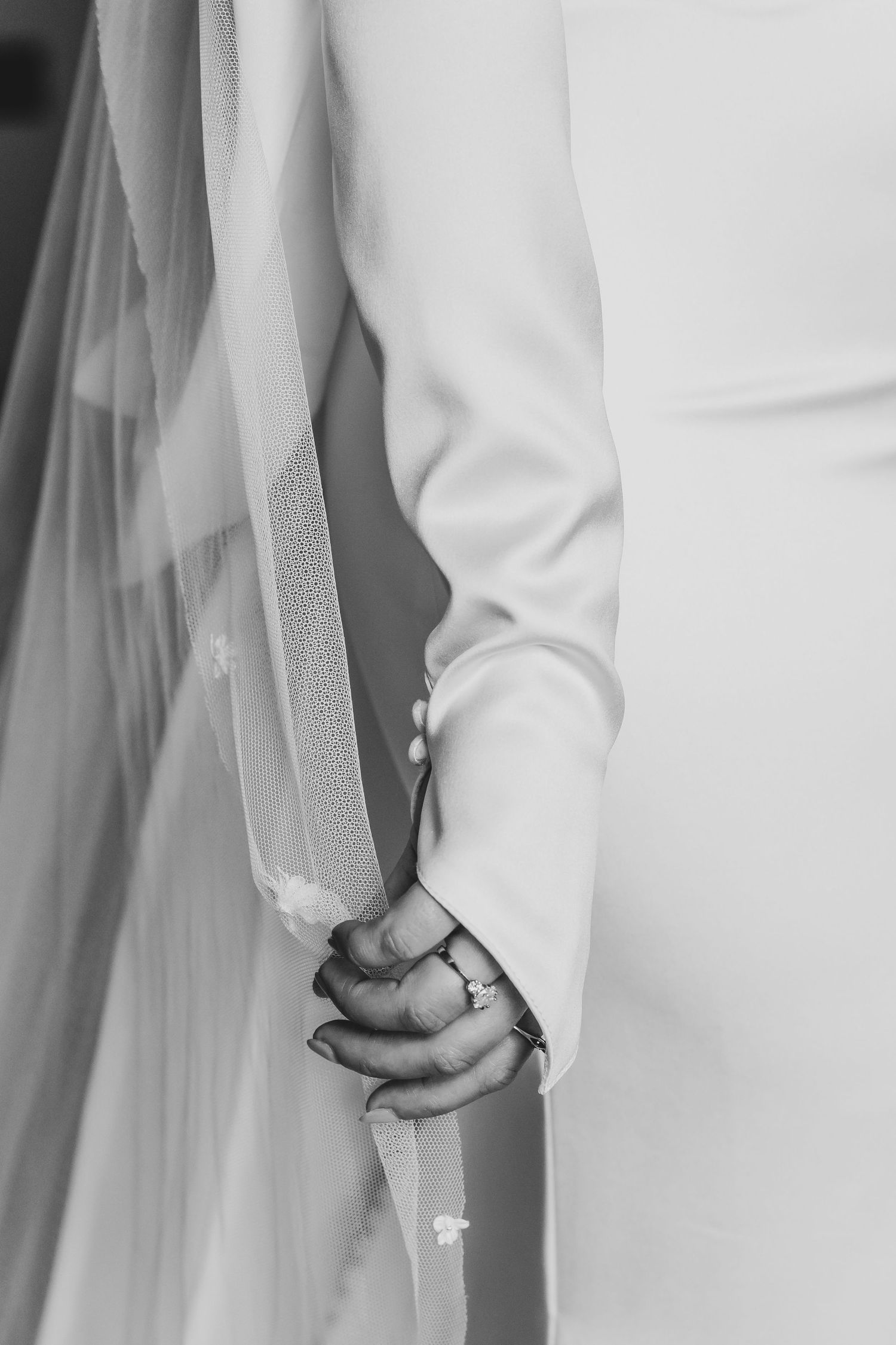 Black and white detail of wedding dress sleeve and veil with rings visible.
