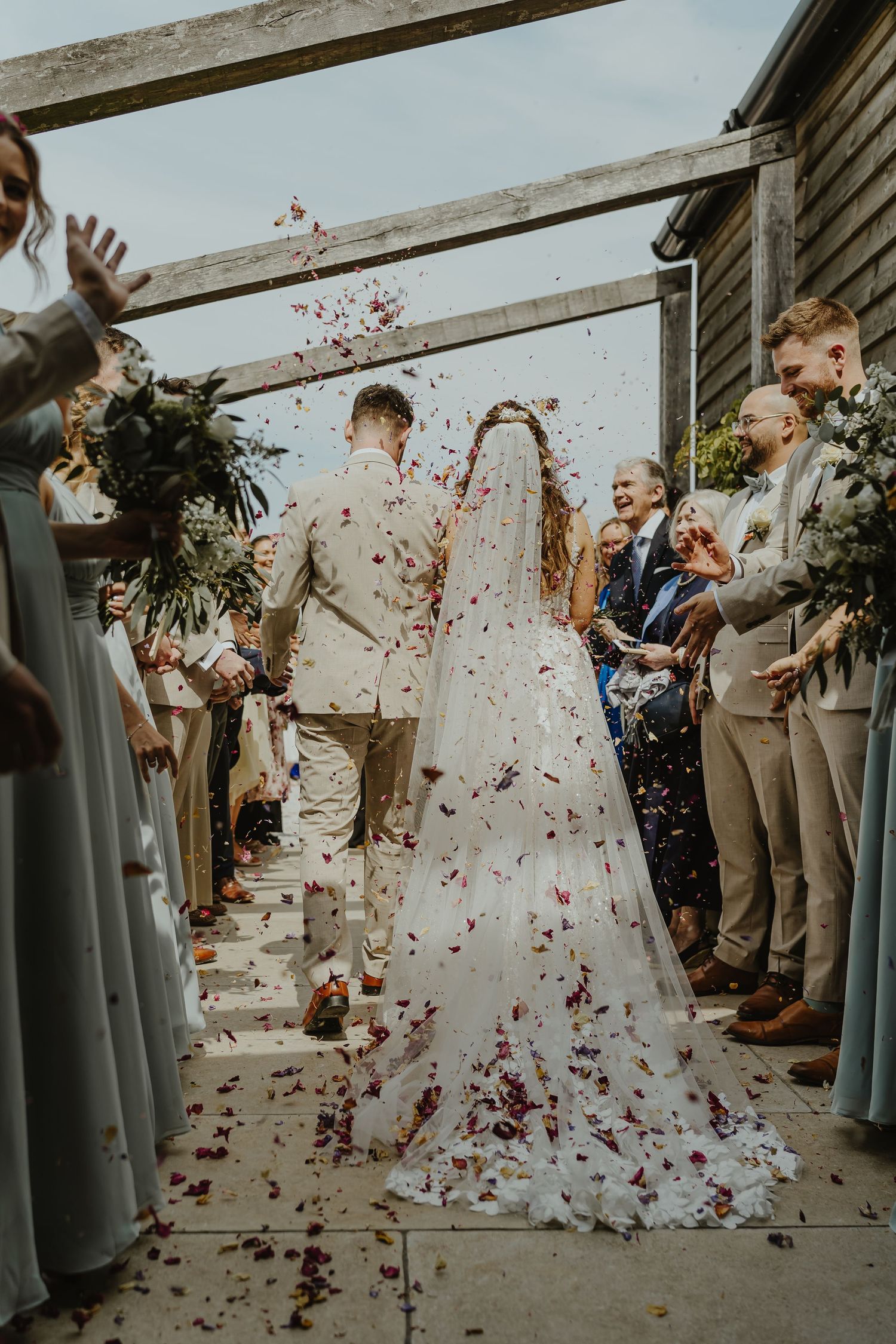 Wedding party stands in line as colorful petals shower down during celebration.