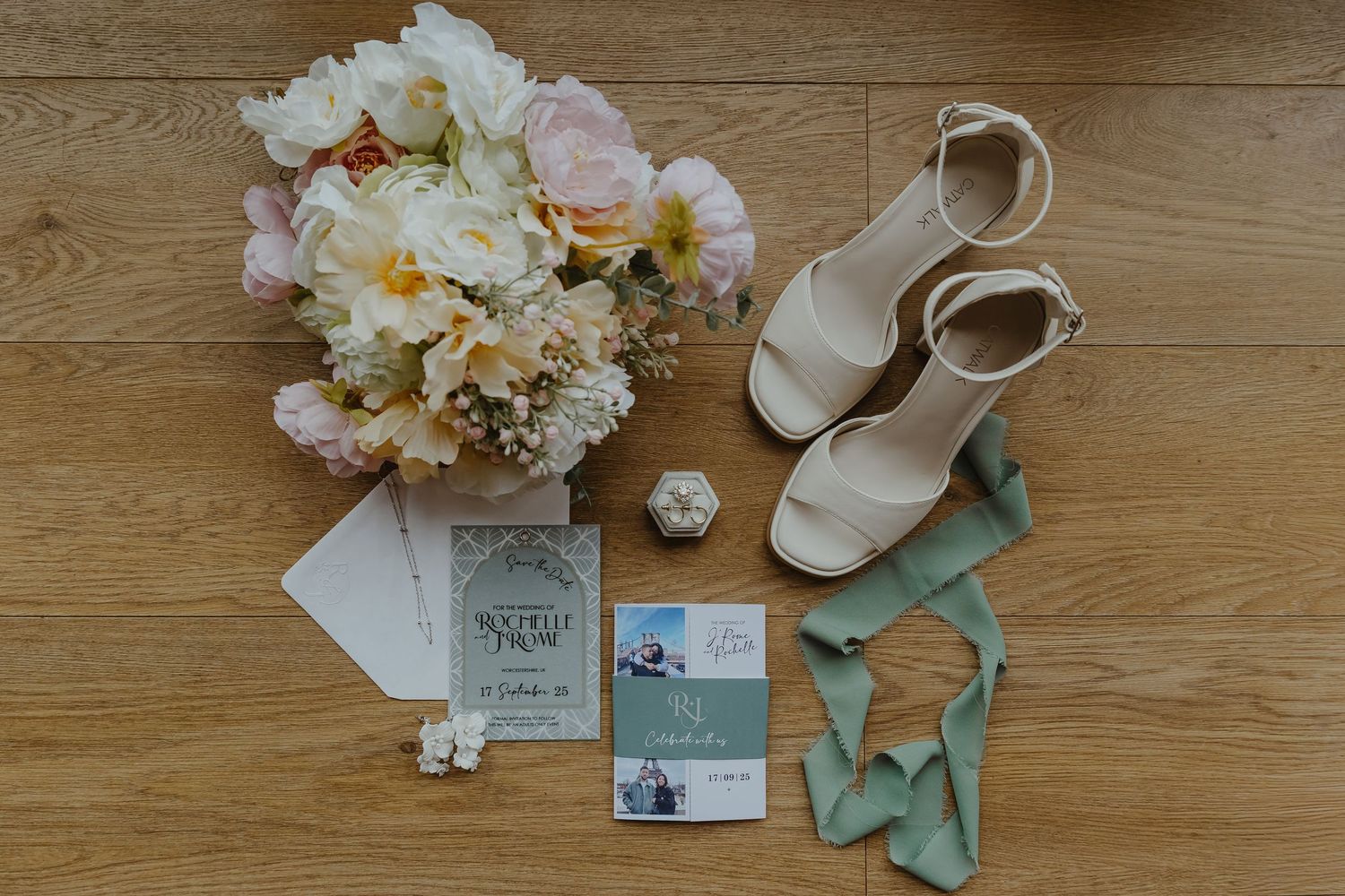 Wedding details including white flowers, shoes and stationery on wooden surface.