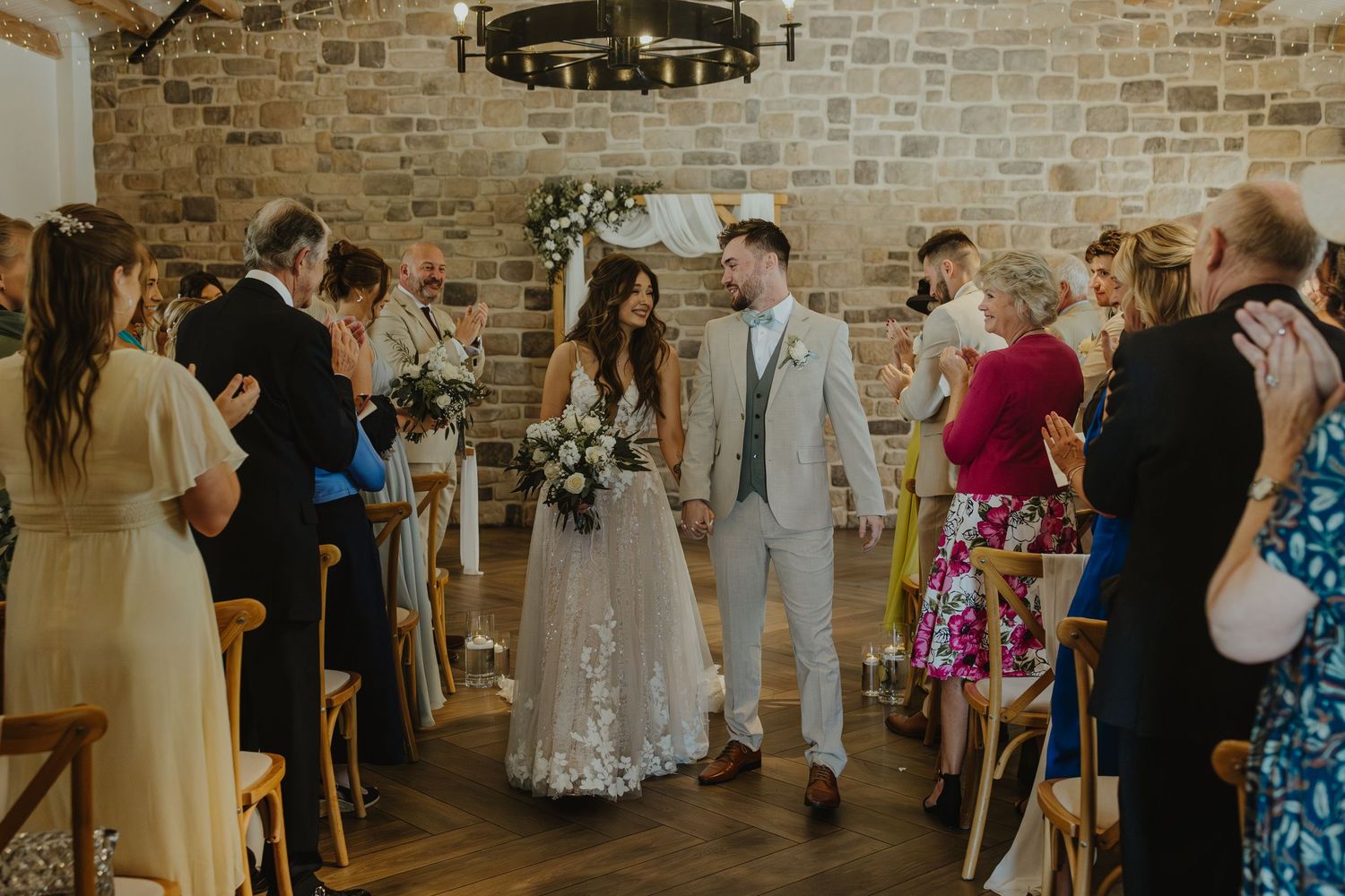 Wedding ceremony in a rustic venue with exposed brick walls and elegant chandelier lighting.