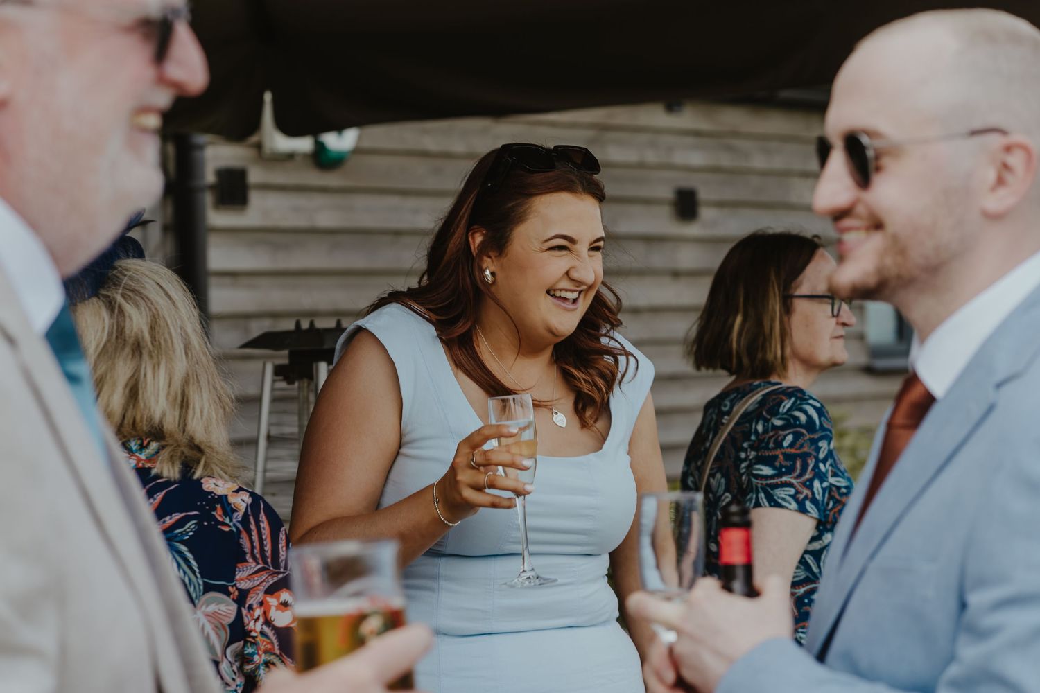 Wedding guests laugh and socialize during outdoor reception.