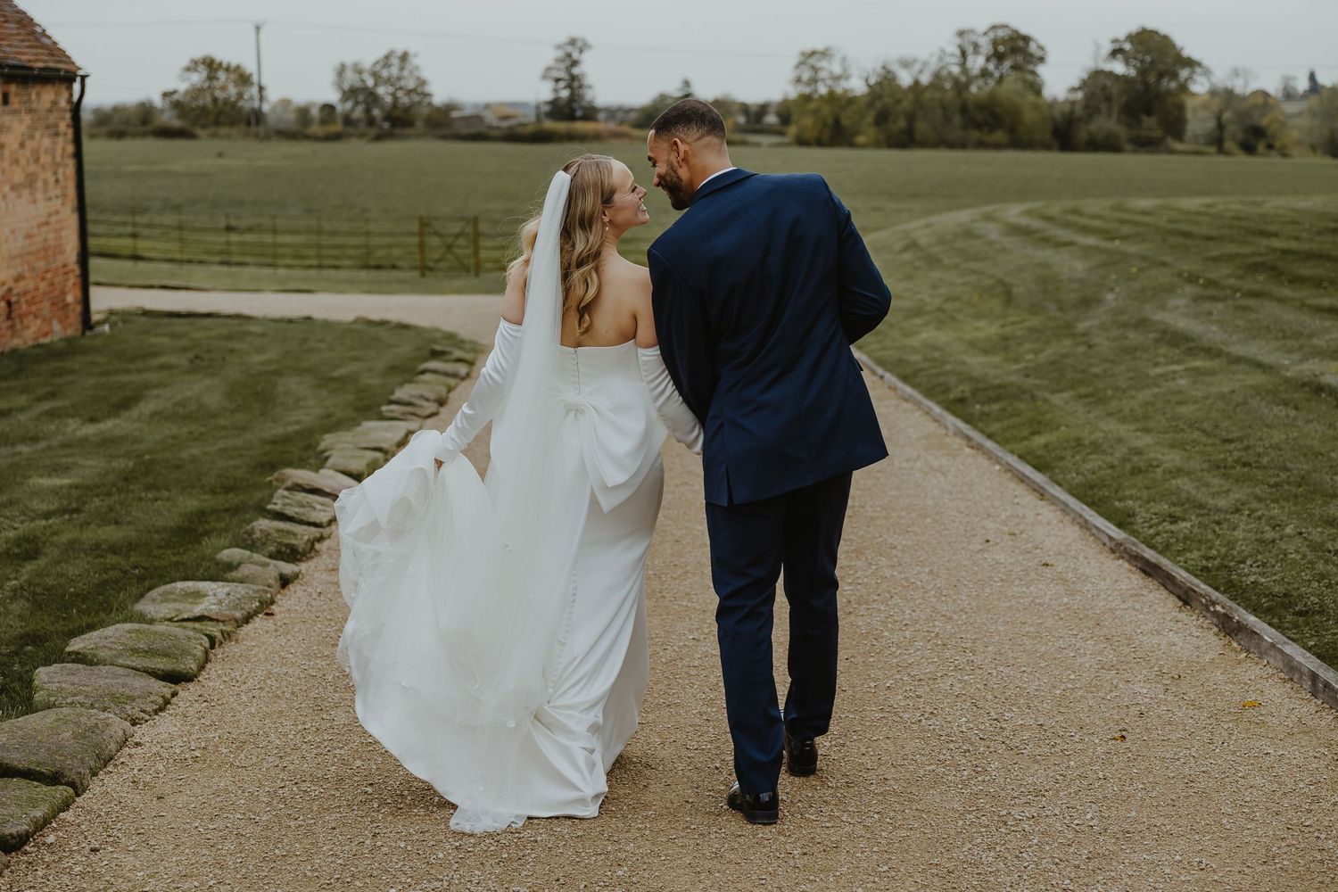 Newlyweds stroll down stone pathway surrounded by manicured grounds.