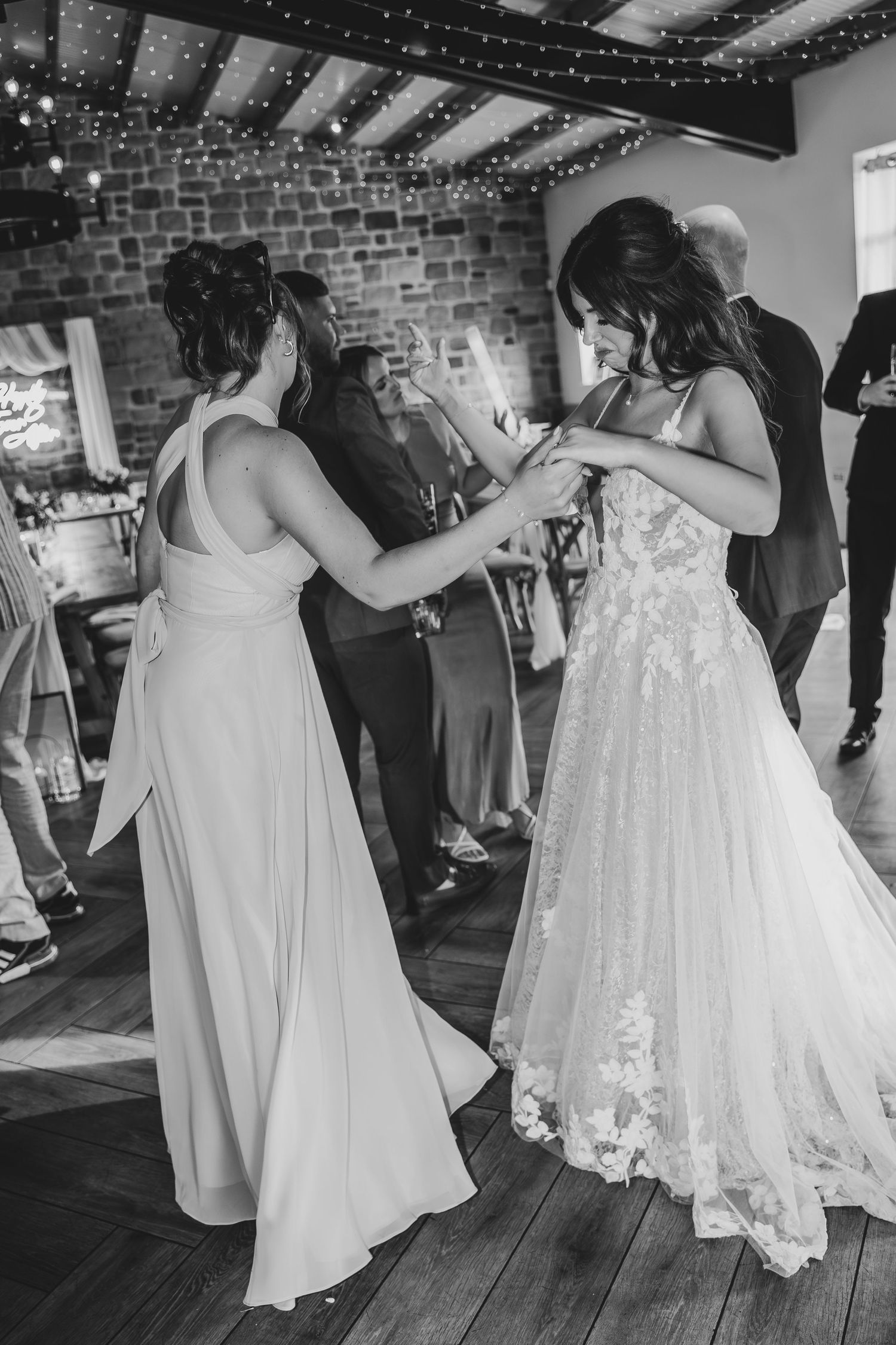 Bridesmaids in light colored dresses dancing with the bride in her white gown.