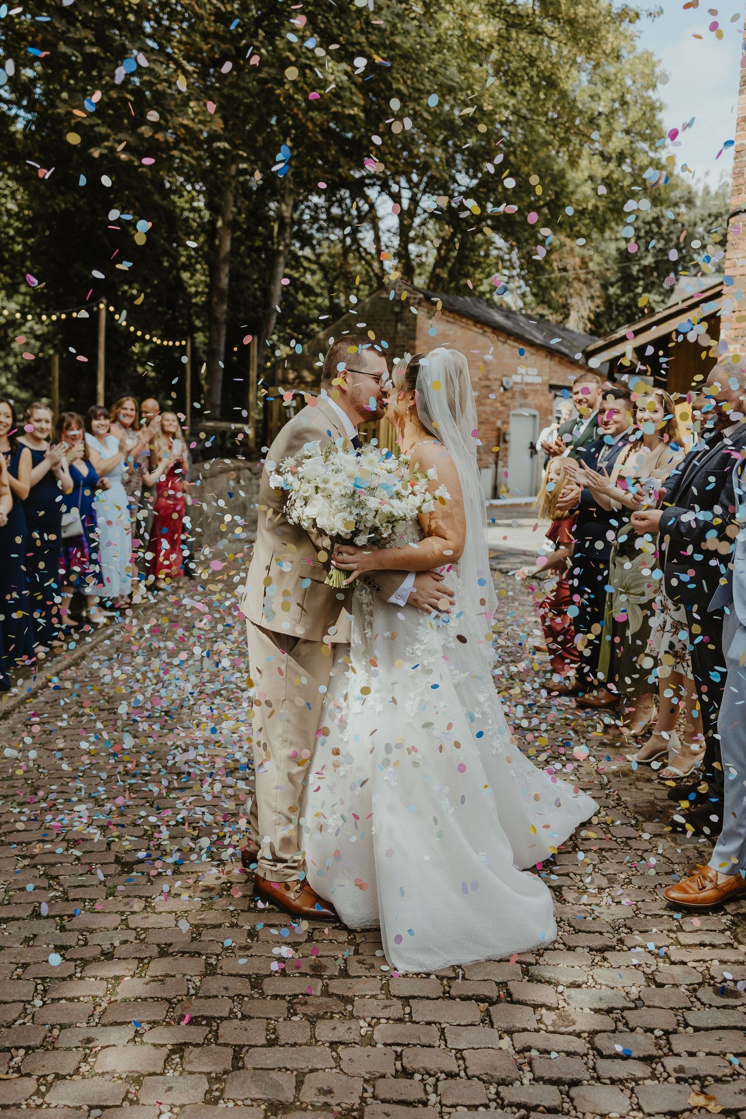 Wedding celebration moment with confetti being thrown on cobblestone path outdoors.