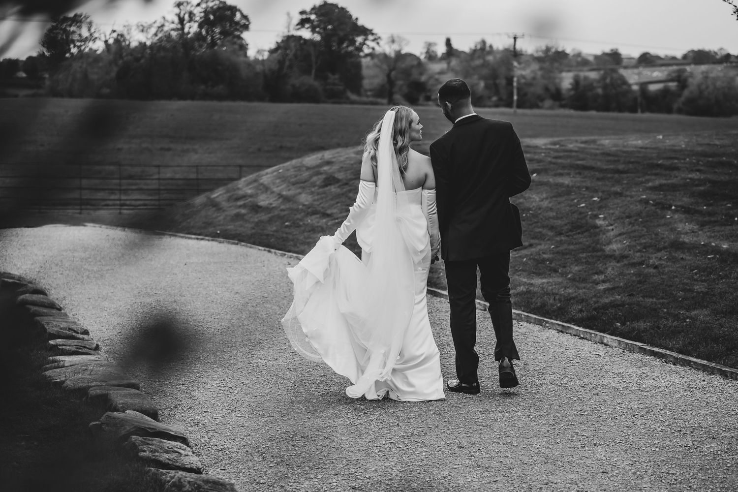 Black and white photo of couple walking down garden path at sunset.
