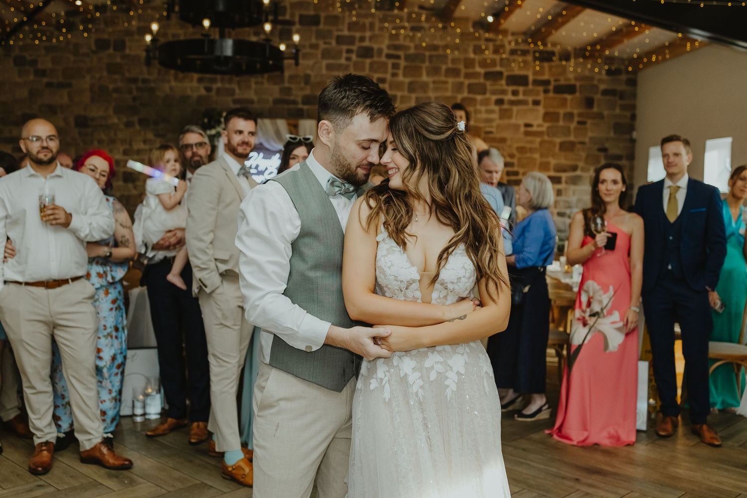 Intimate first dance moment in a rustic brick-walled venue with string lights overhead.