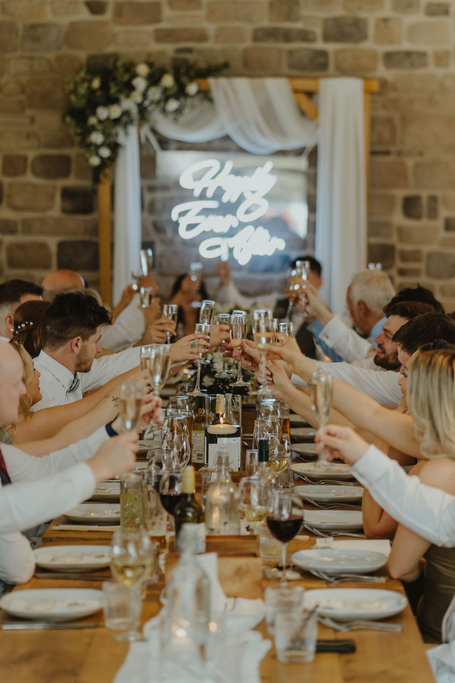 Wedding guests raise their glasses in a toast at long reception table.