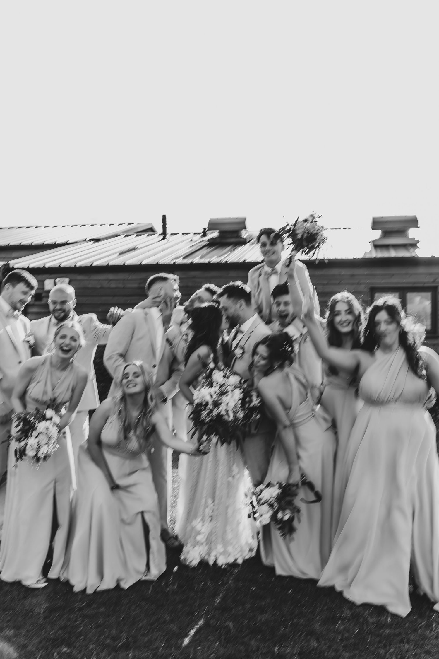 Black and white photo of wedding party celebrating outdoors with natural expressions.