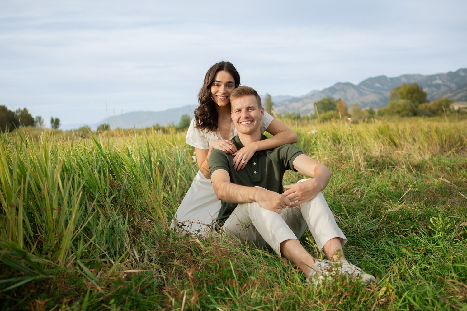 A newly engaged Montana Couple sit together in front of the Bridger Mountains in Bozeman, Montana.