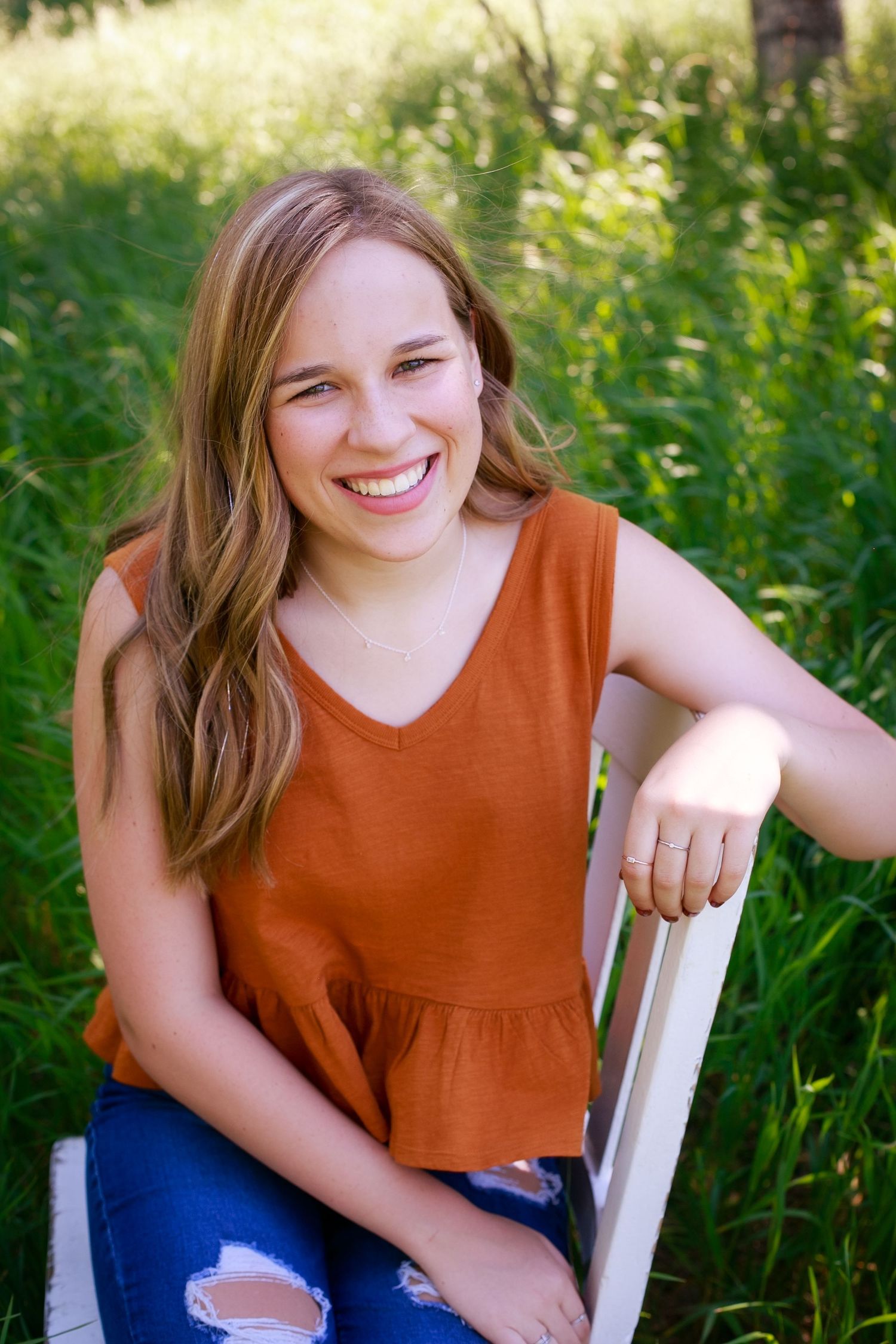 Image of Sierrah Elizabeth sitting on a white chair for her own high school senior photos. Image by Megan Lane Photography
