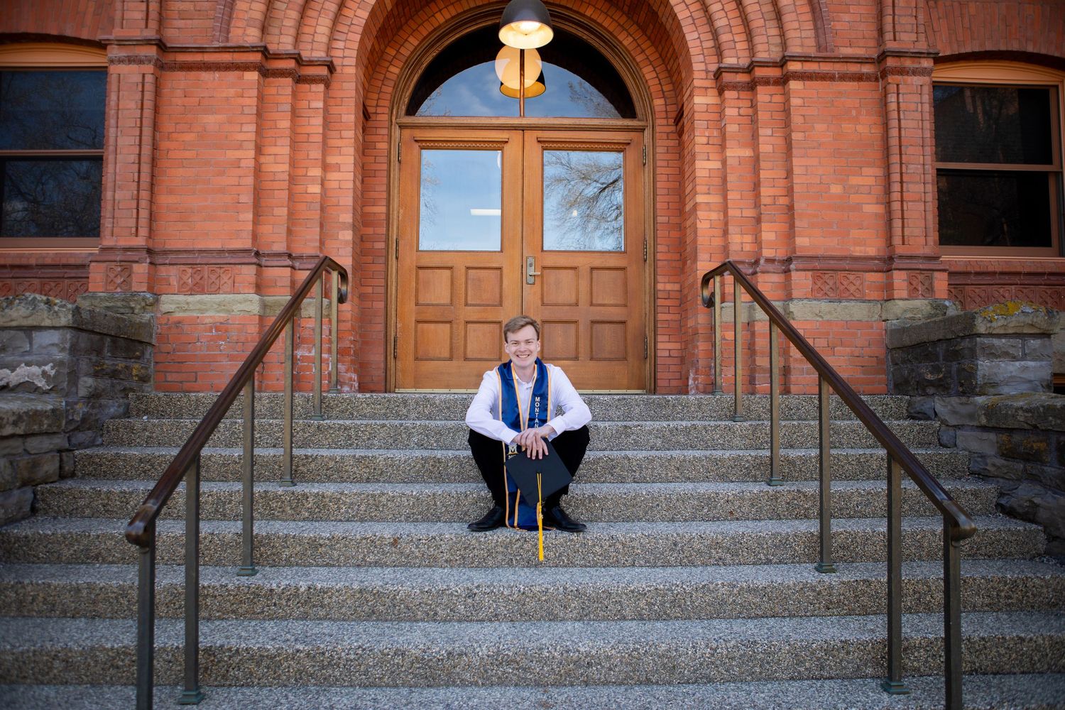A Montana State University Grad sits on the steps on Montana Hall in Bozeman, Montana.