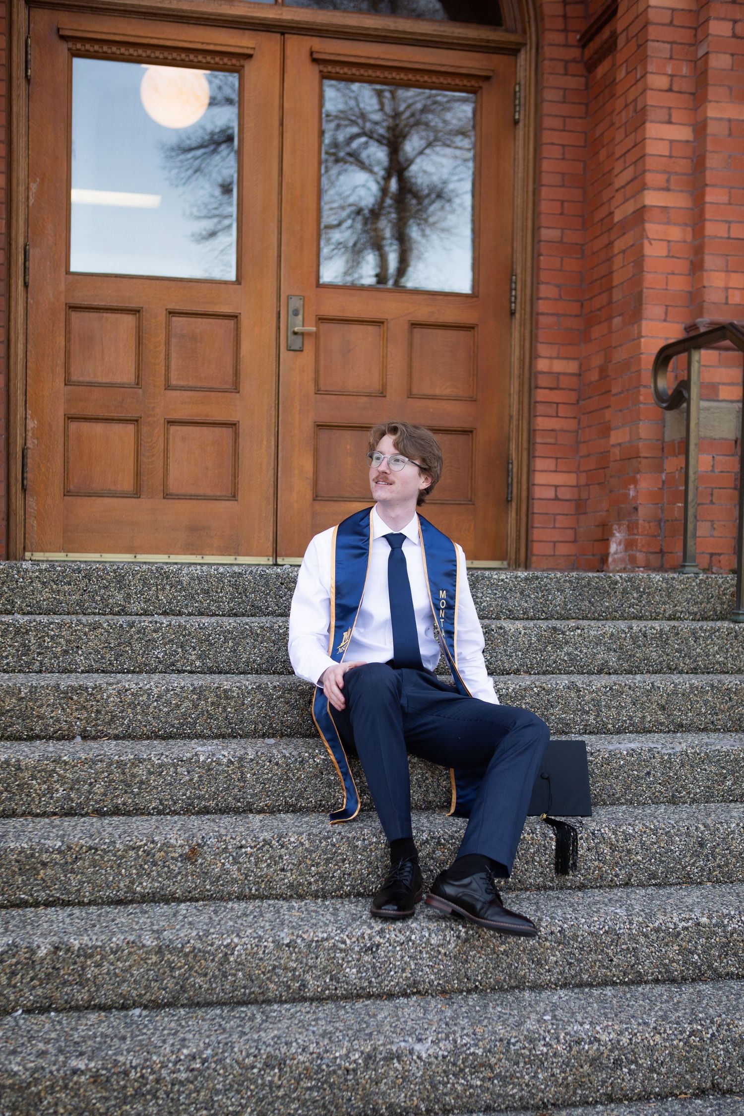 A Montana State University grad sits on the steps on Montana Hall in Bozeman.