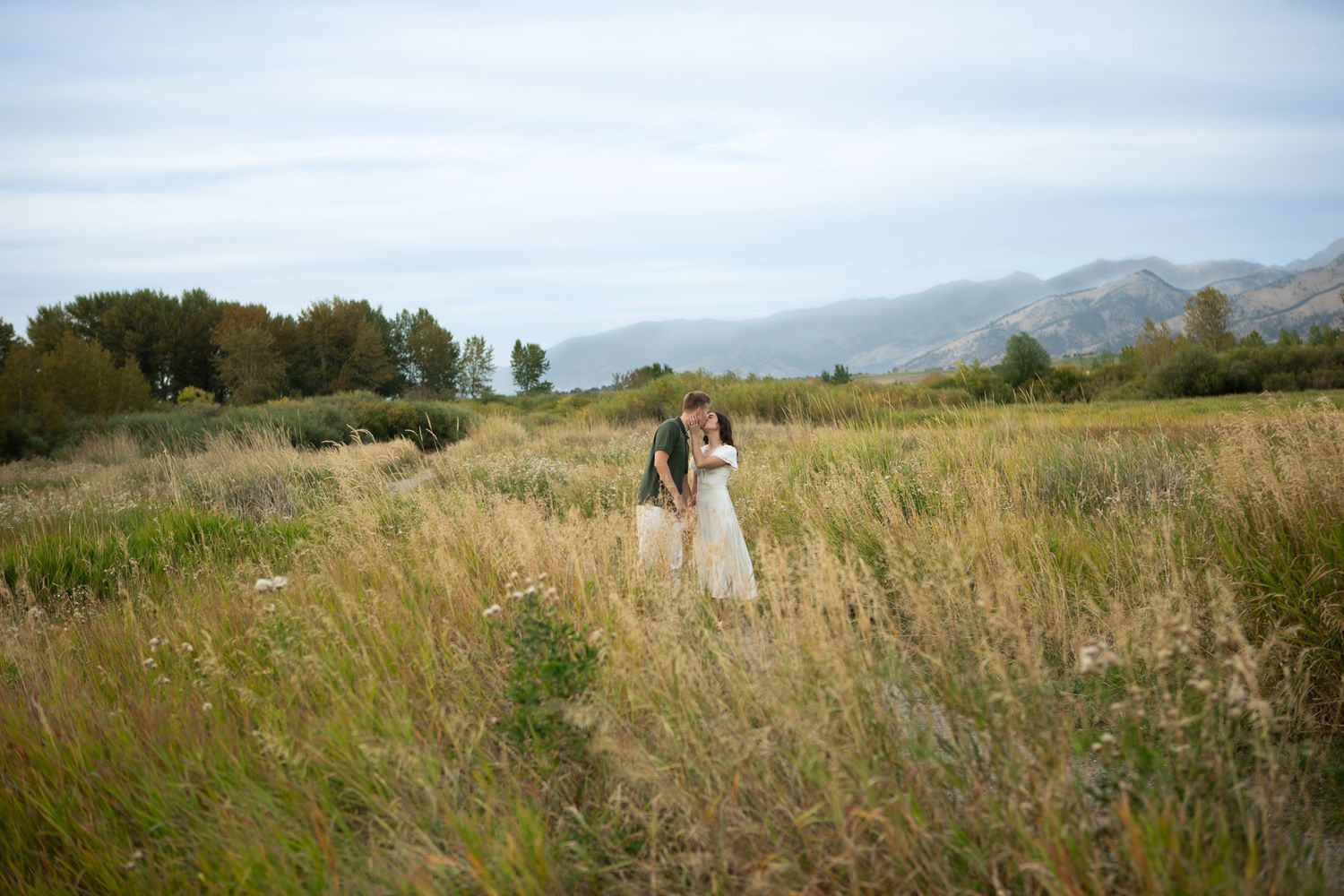 A newly engaged Montana Couple kiss in a field in Bozeman, Montana for their engagement photos.