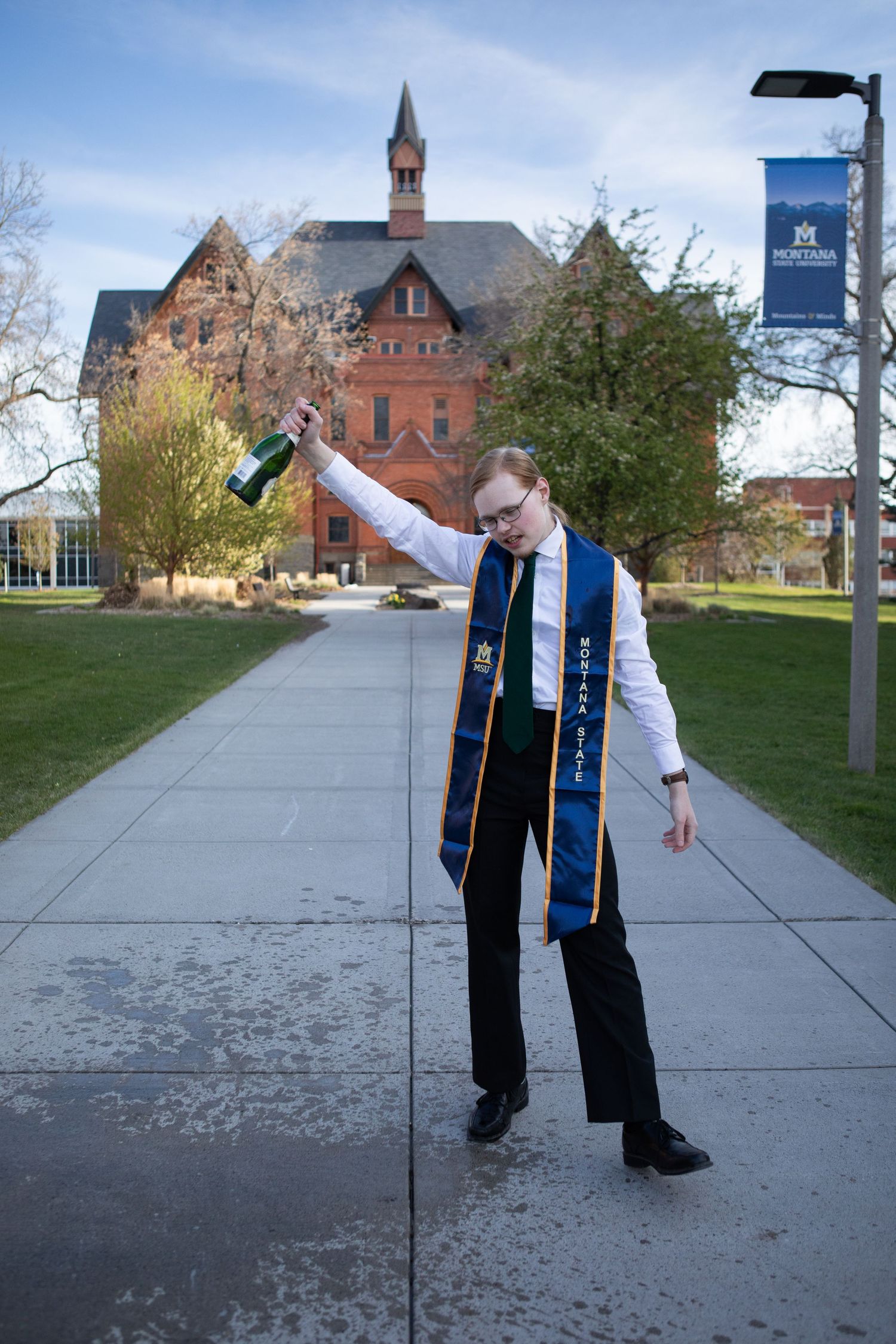 A Montana State University Grad holds up a bottle of champagne in celebration in front of Montana Hall.