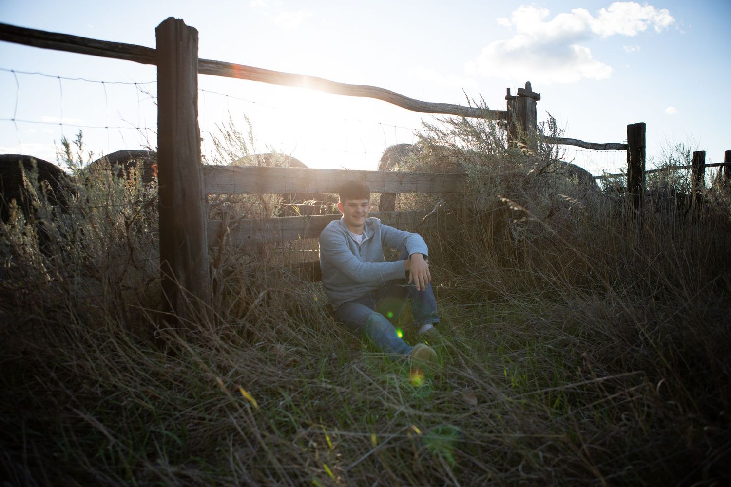 A Bozeman Senior sitting up against a fence with the sunset in the background