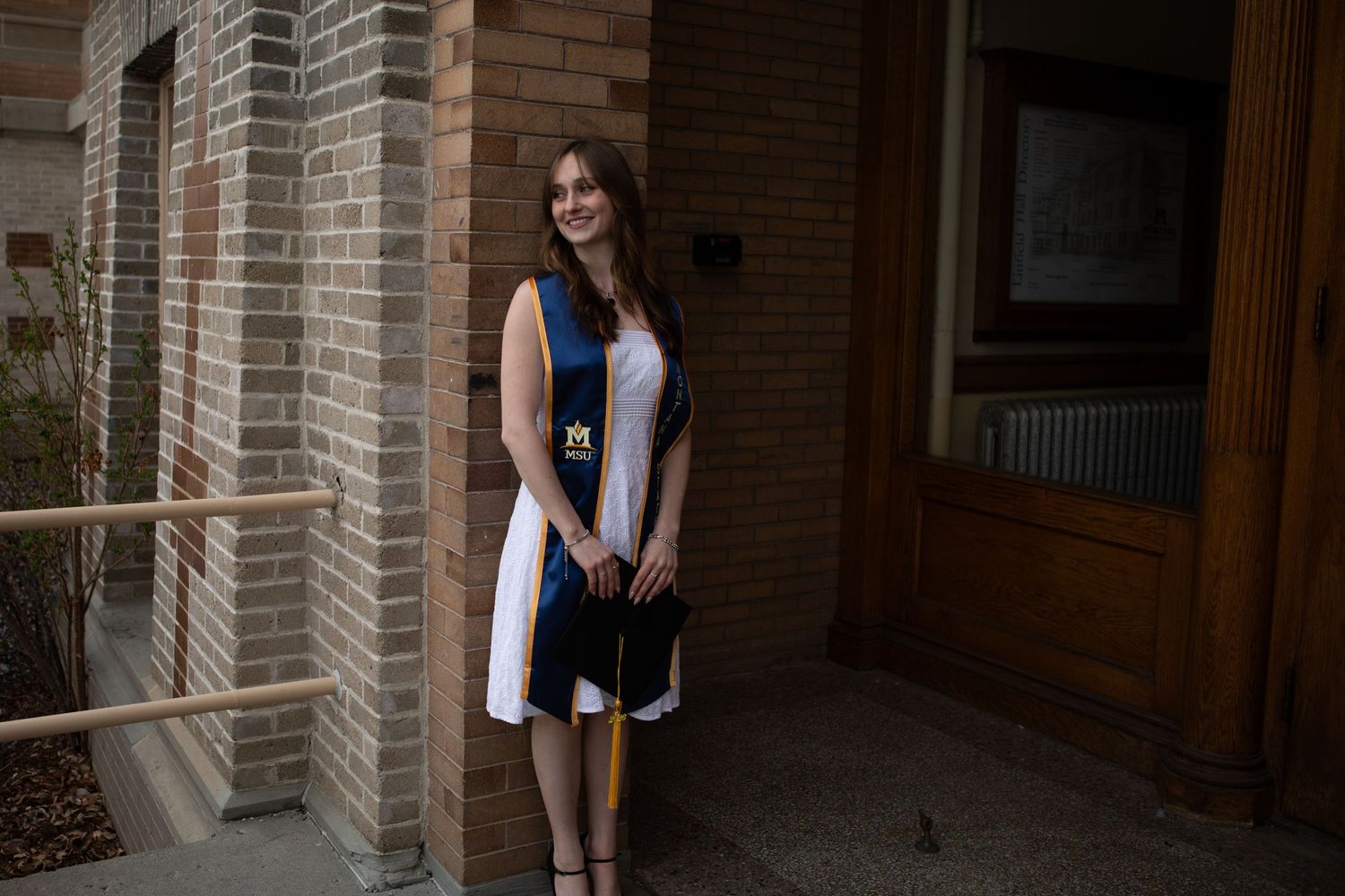 A Montana State University Graduate stands with her cap against Linfield Hall in Bozeman, Montana.