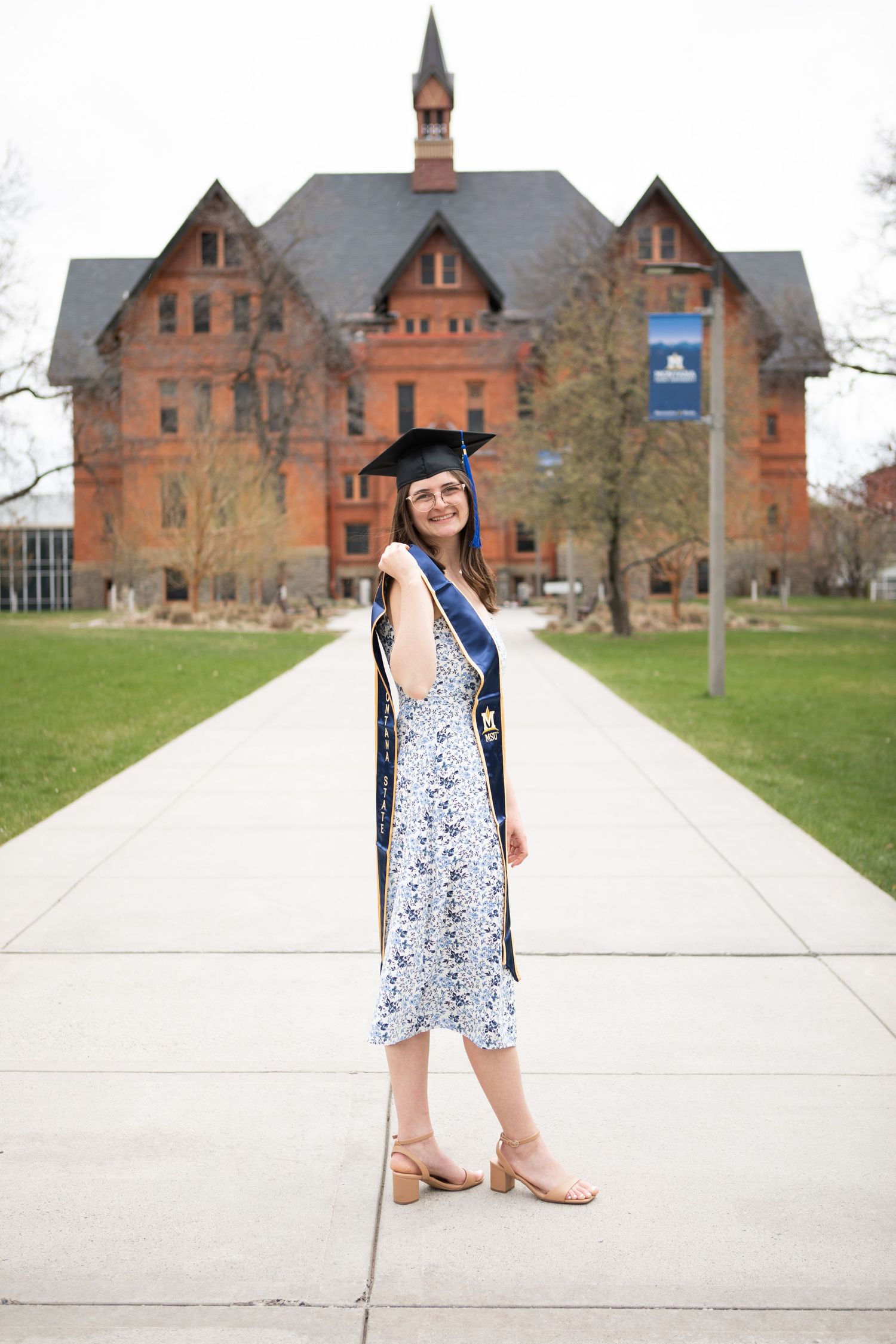 A Montana State University Grad stands in front of Montana Hall in Bozeman, Montana.