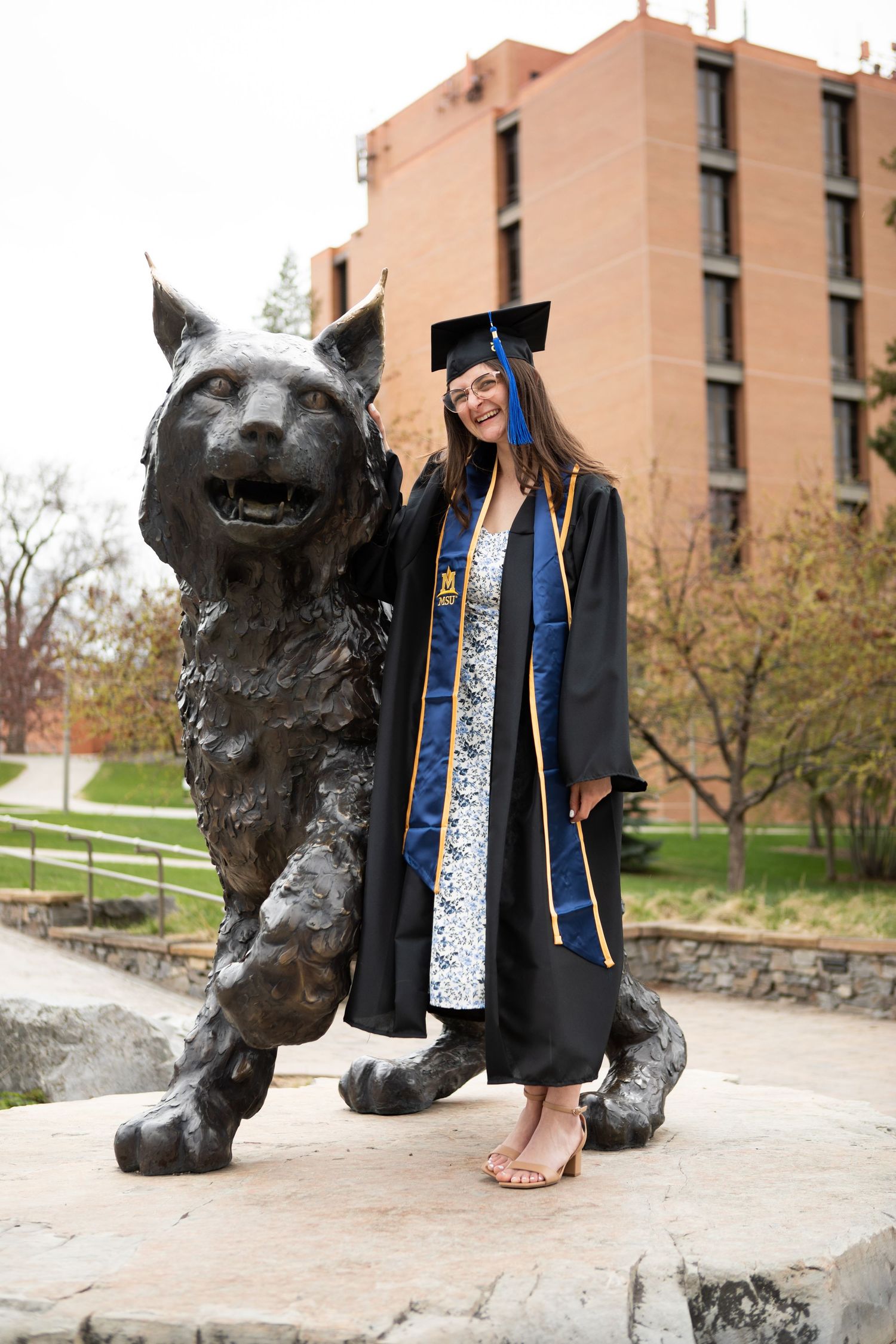 A Montana State University grad stands next to Spirit the Bobcat on Campus in Bozeman.