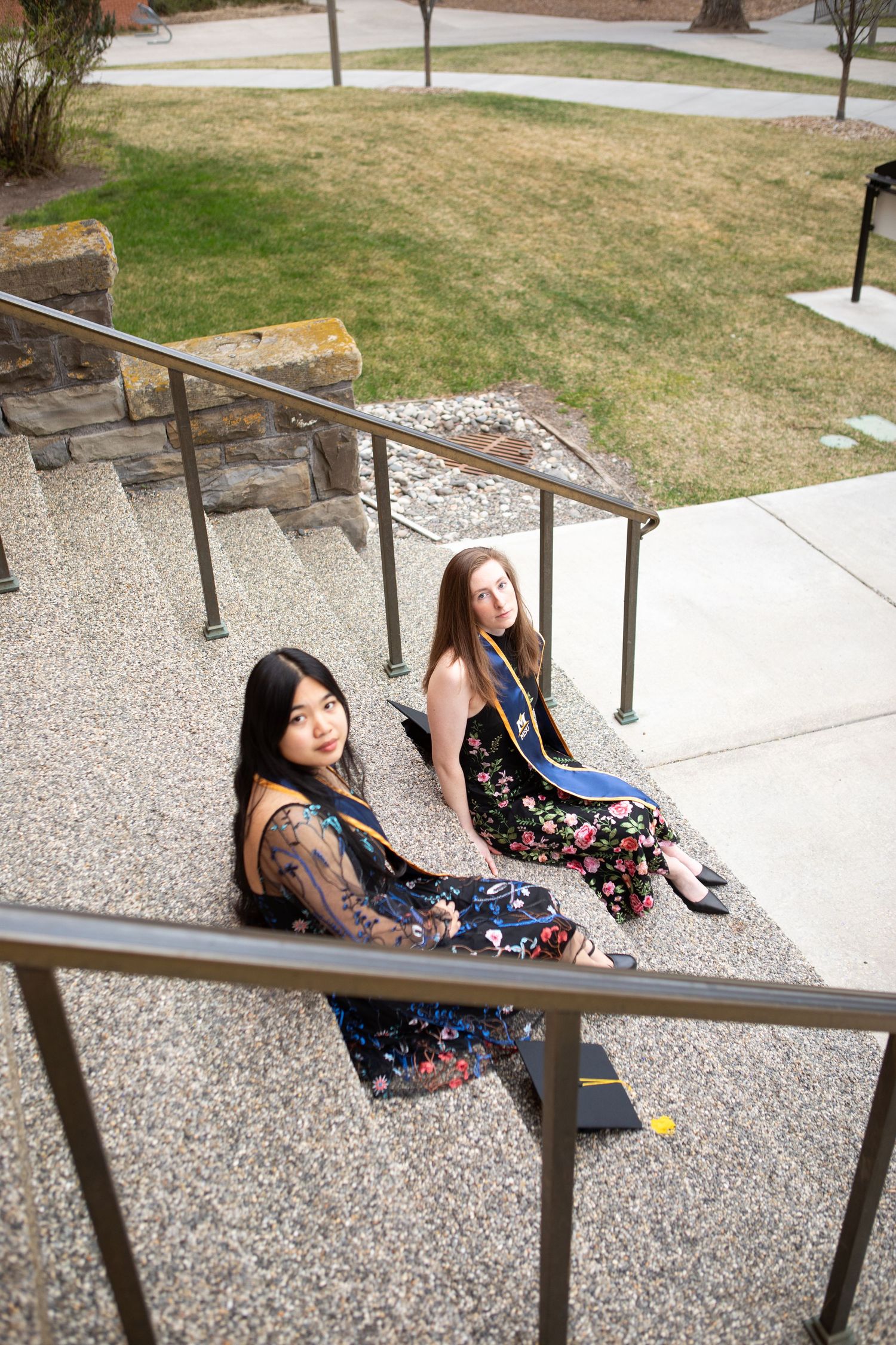Two Montana State University Grads sit on the steps of Montana Hall in Bozeman, Montana.