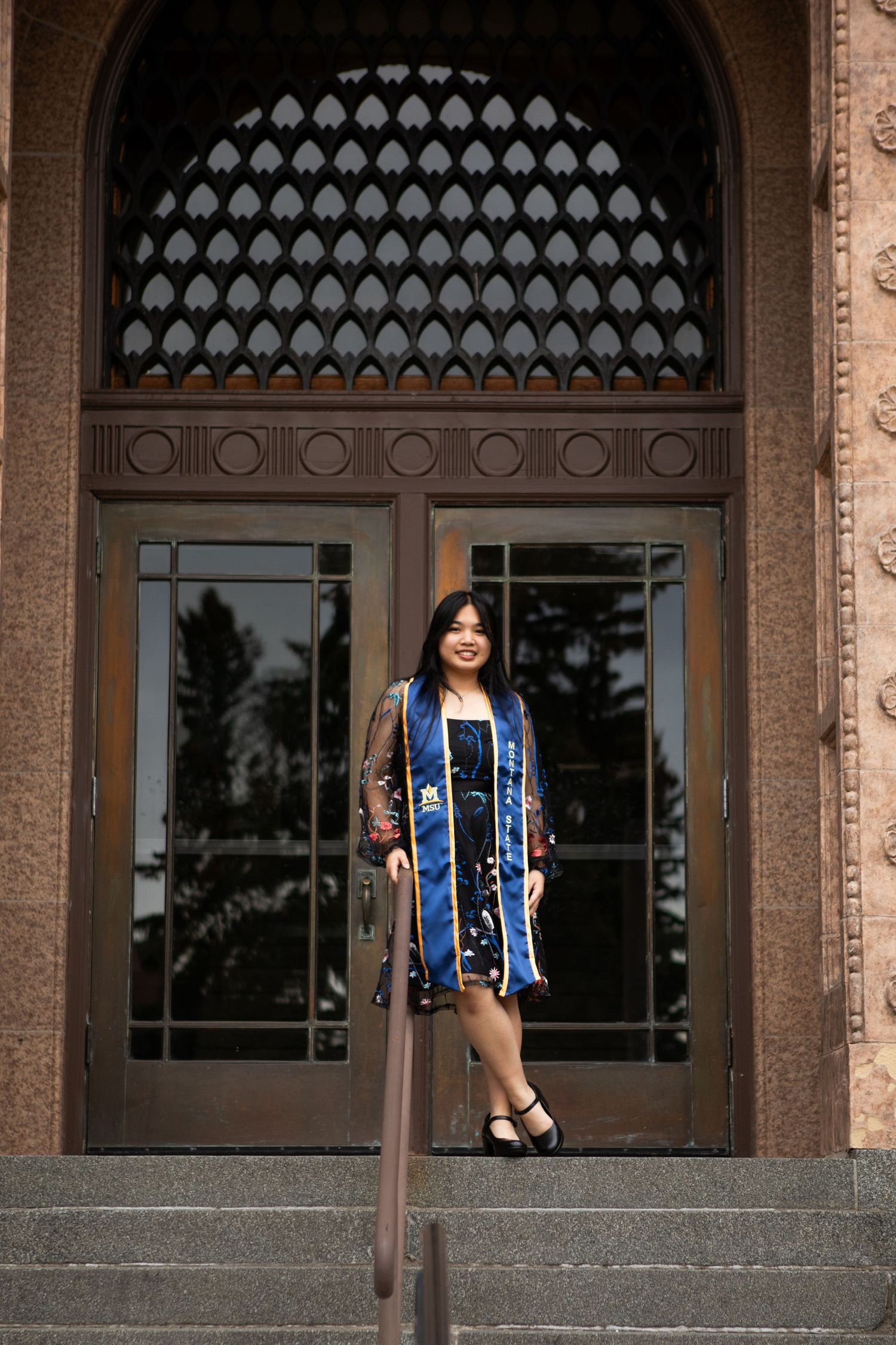 A Montana State University Grad stands on the steps of Lewis Hall in Bozeman, Montana.