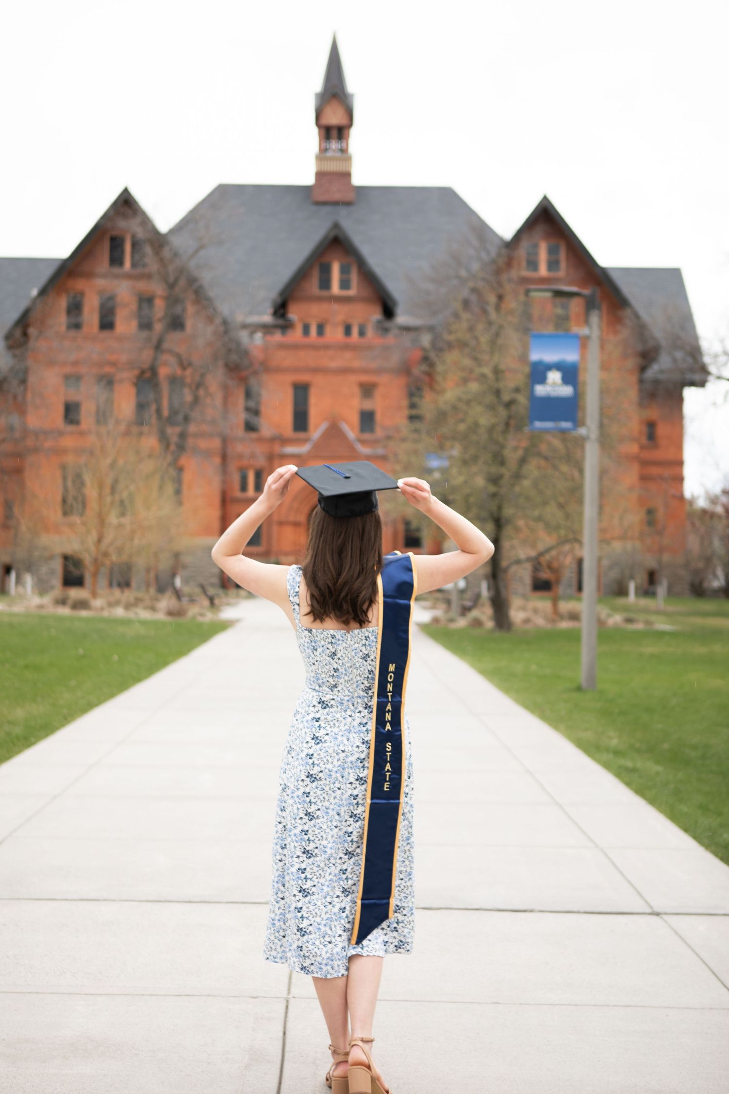 A Montana State University Grad holding her cap in front of Montana Hall.