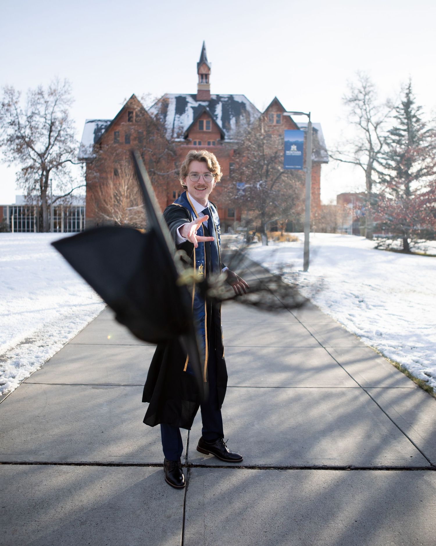 A Montana State University grad throws his cap in front of Montana Hall in Bozeman.