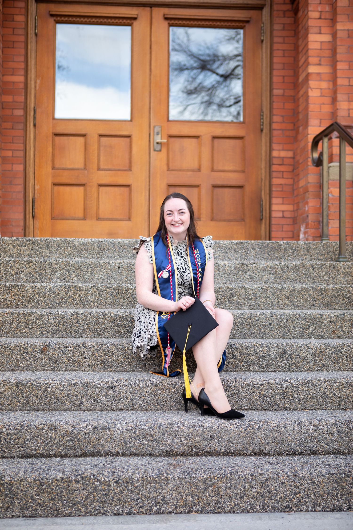 A Montana State University Grad sits on the steps of Montana Hall in Bozeman, Montana.