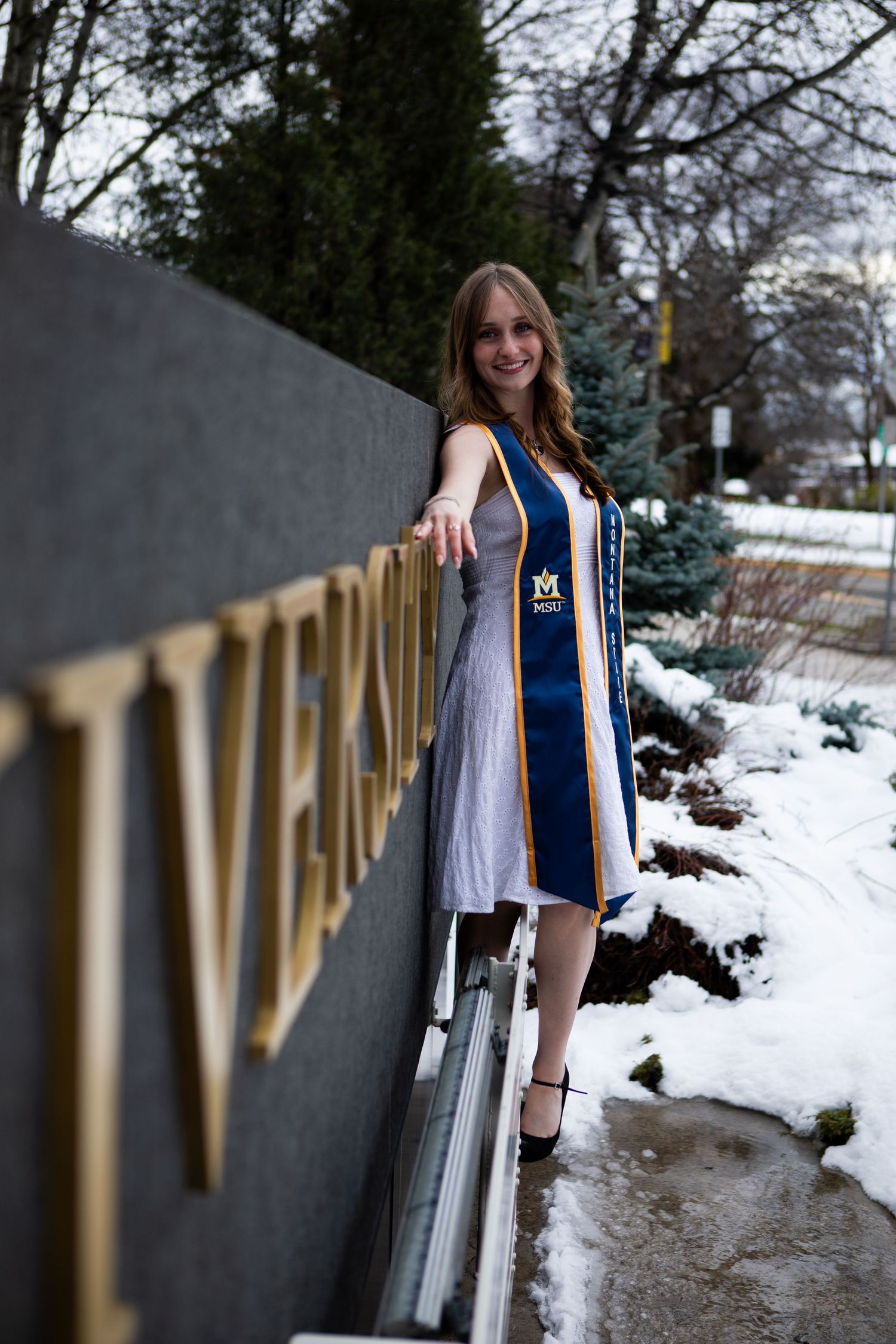 A Montana State University Grad stands in front of the welcome sign on campus in Bozeman, Montana.