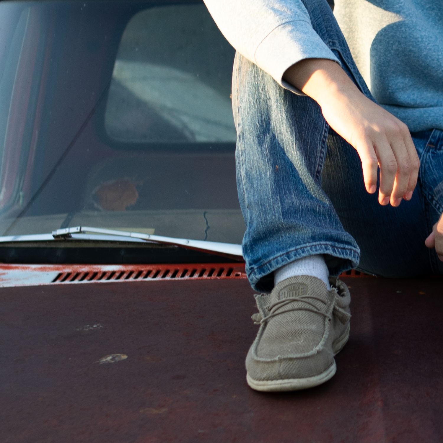 Detail image of a Montana Senior sitting on a old Ford truck, shows his leg and arm