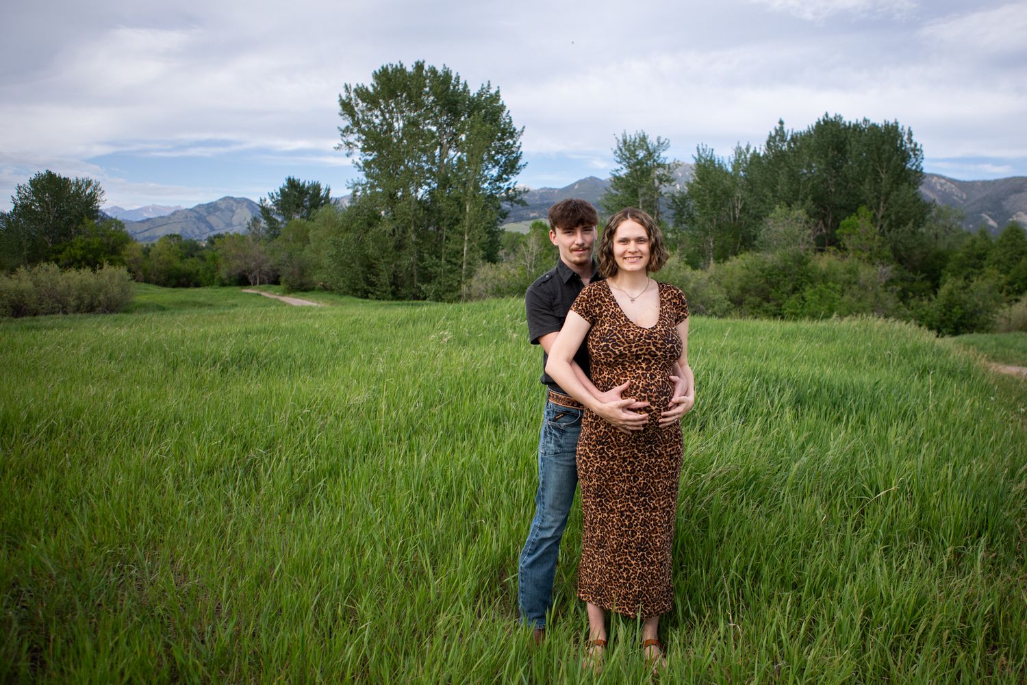 A Montana couple stands in a field in front the mountains for a maternity session.