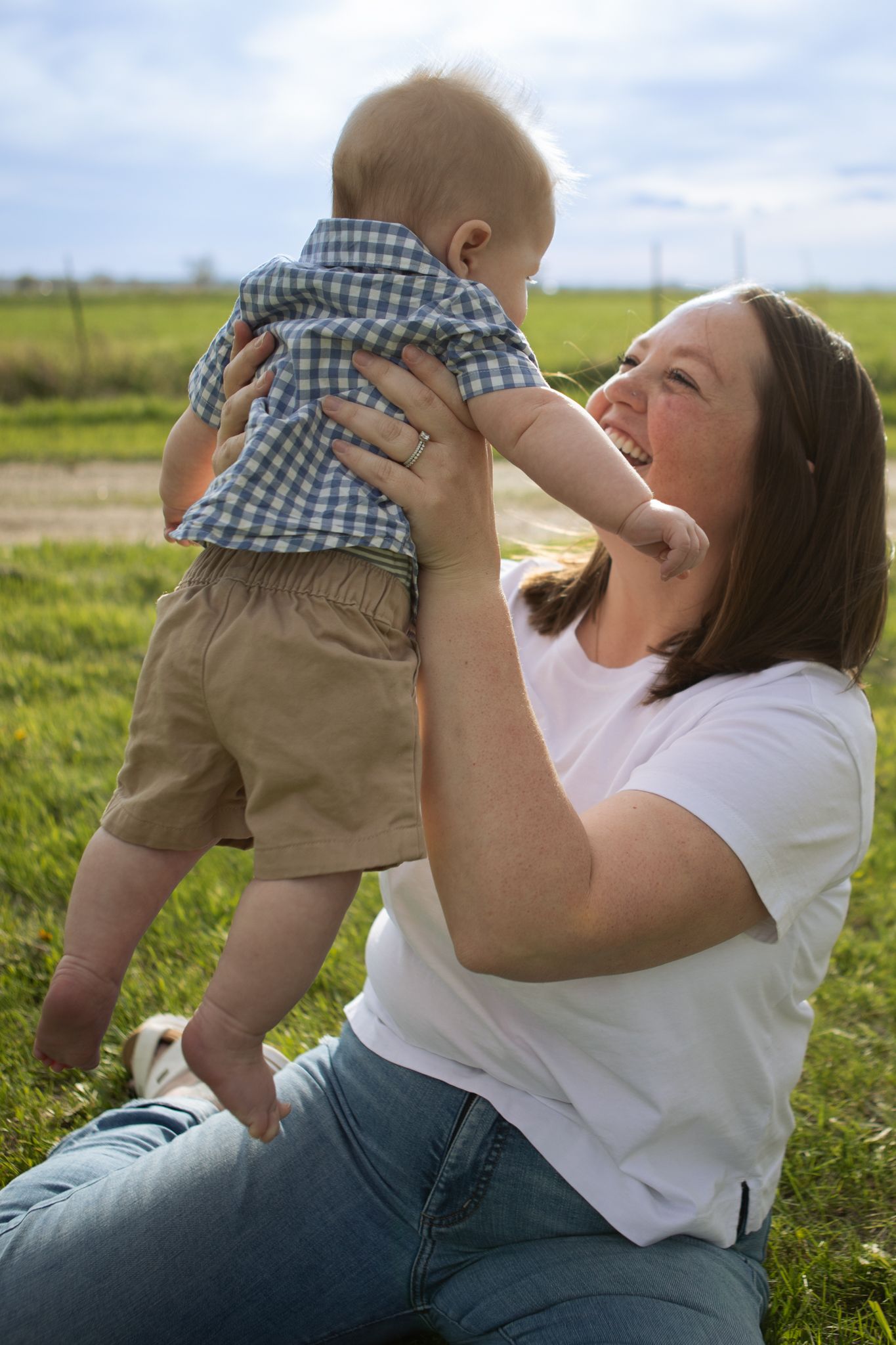 A Bozeman mom holding up her baby in a field.