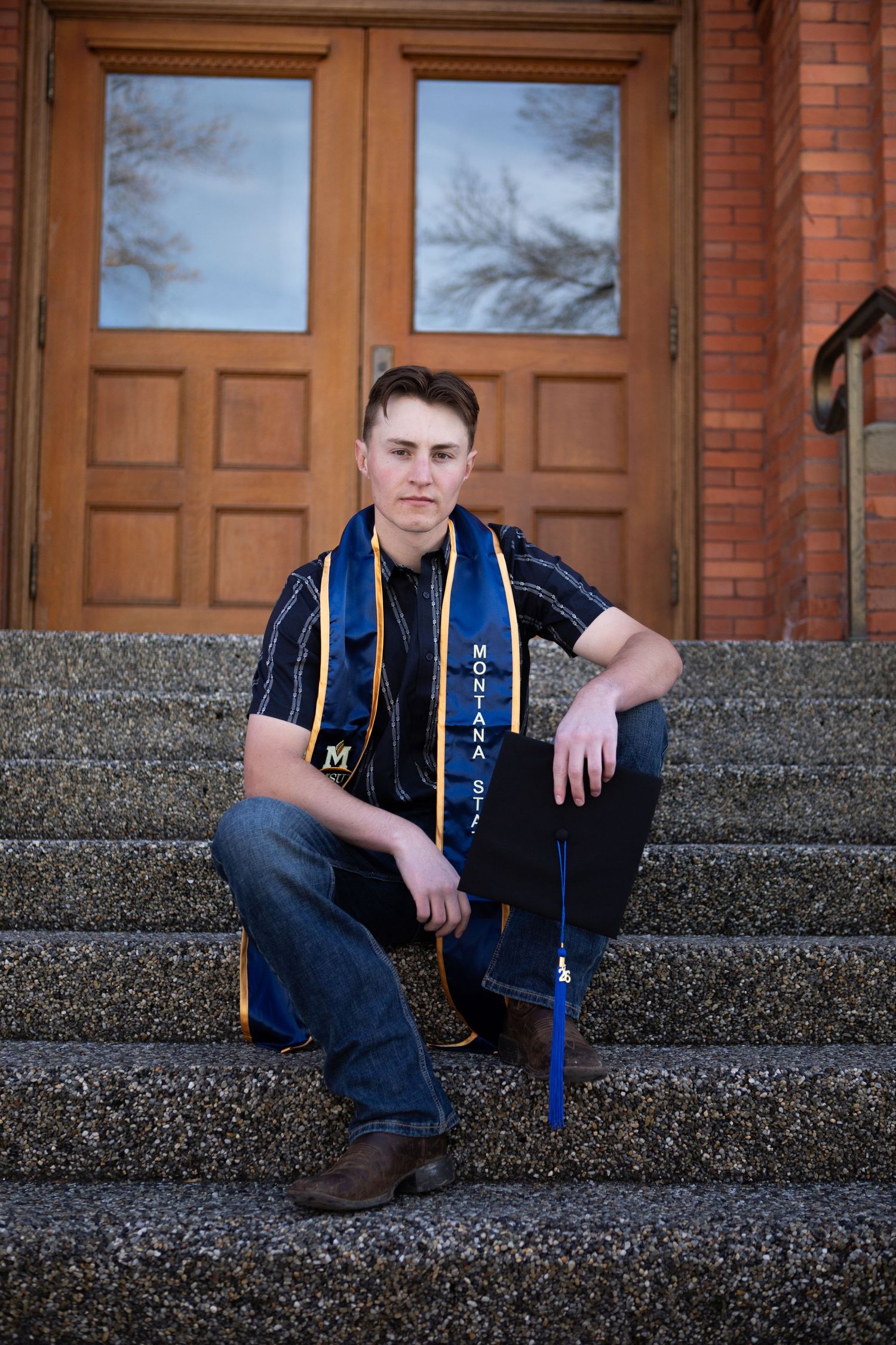 A Montana State University Grad sits on the steps of Montana Hall in Bozeman, Montana.