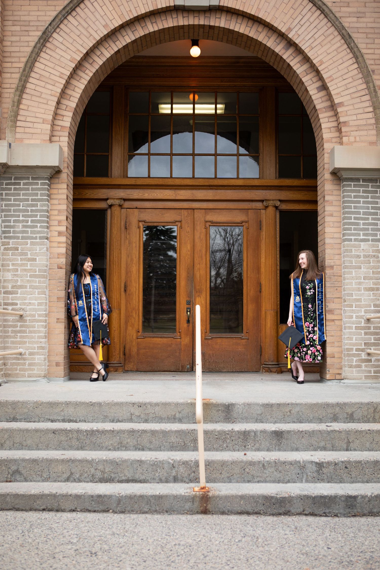 Two Montana State University Grads stand against Linfield Hall in Bozeman, Montana.