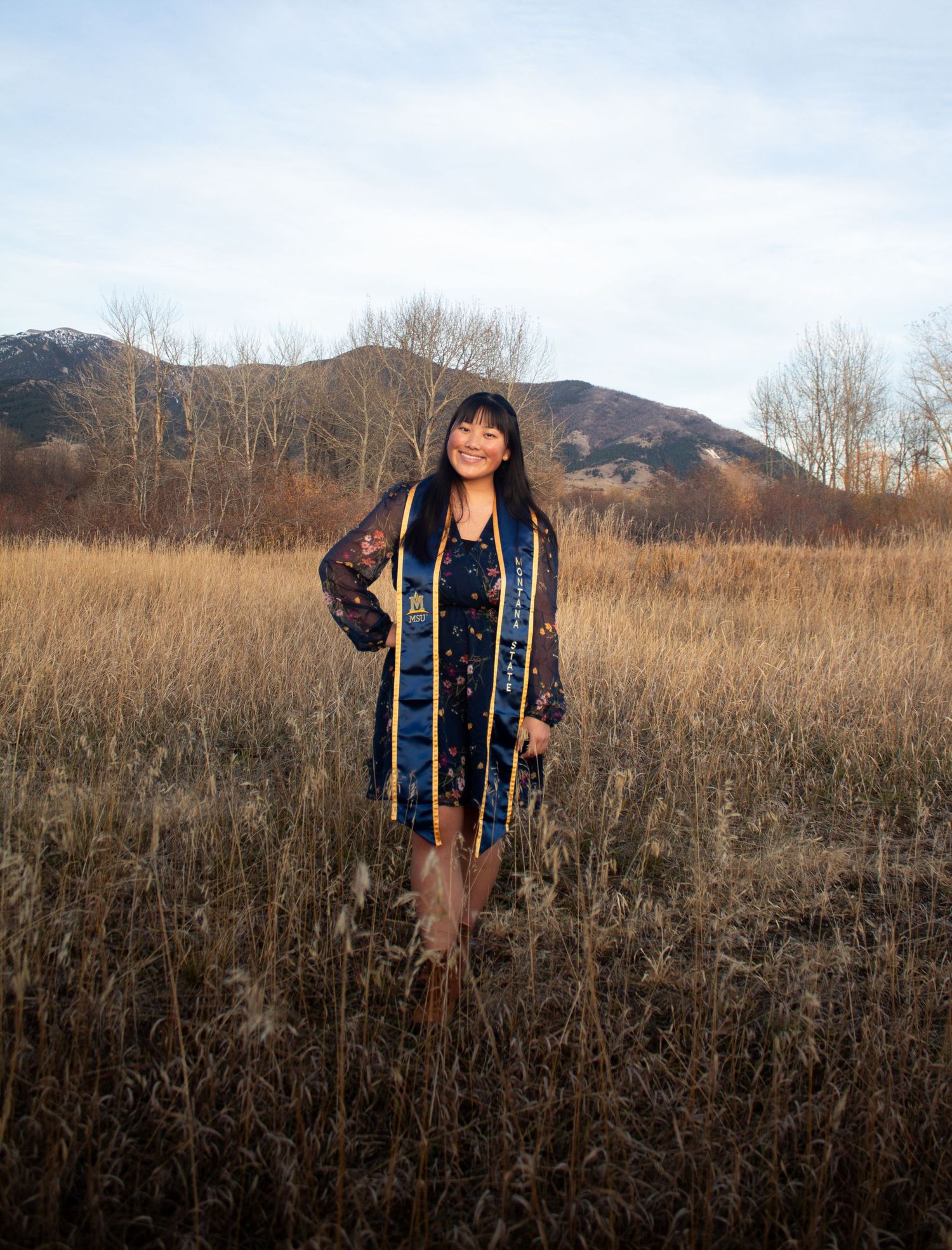 A MSU grad standing in front of the Bridge Mountains and the M in the Gallatin Valley.