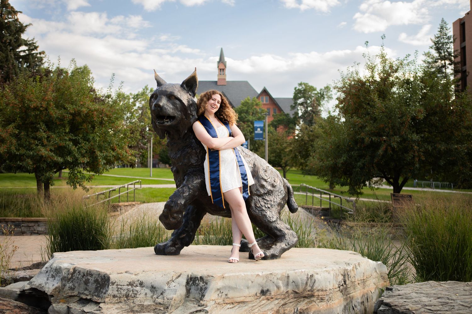 A Montana State Grad is leaning up against Spirit the Bobcat on campus in Bozeman, Montana.