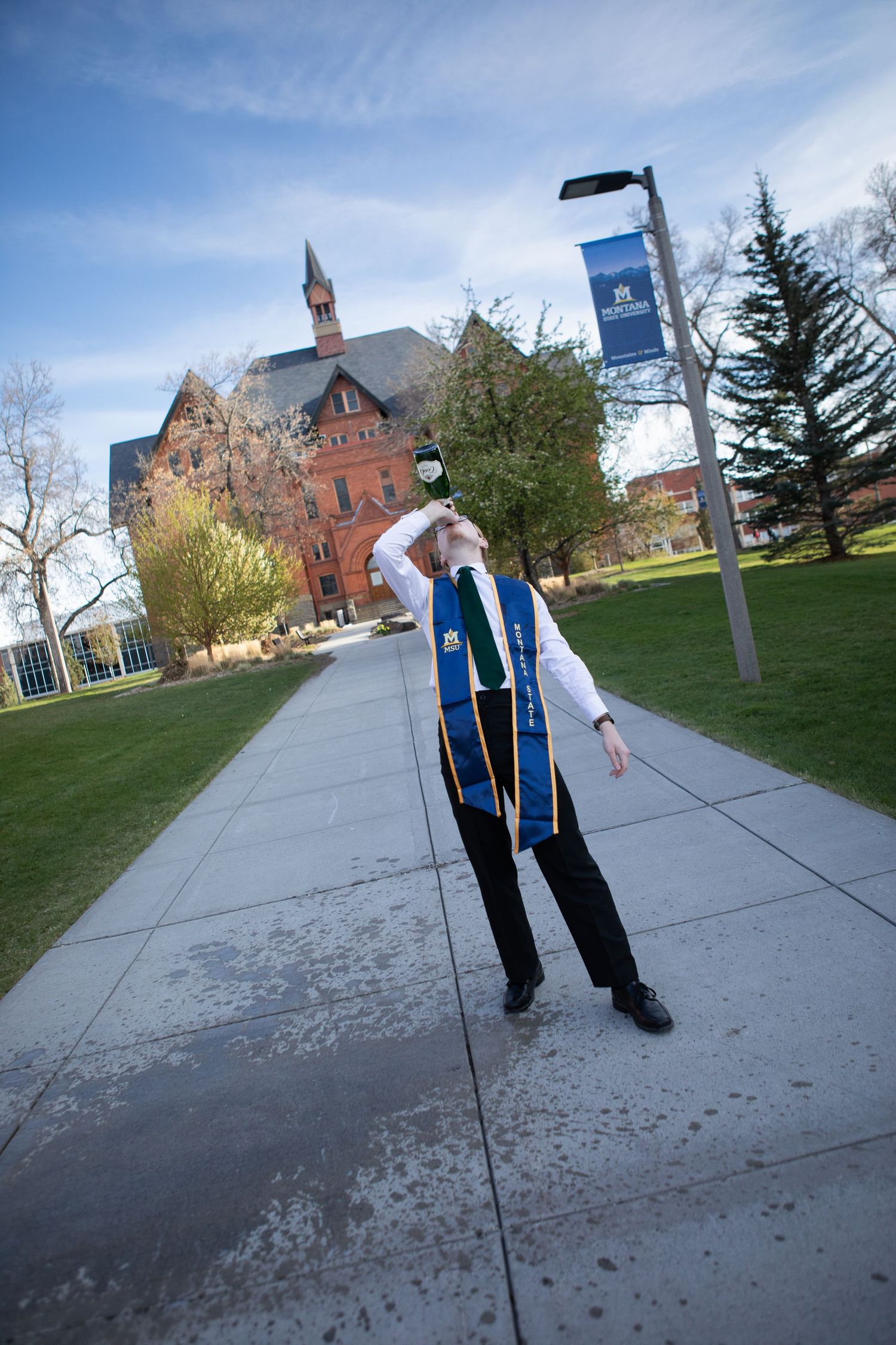 A Montana State University Grad drinks a bottle of champagne in front of Montana Hall in Bozeman, Montana.
