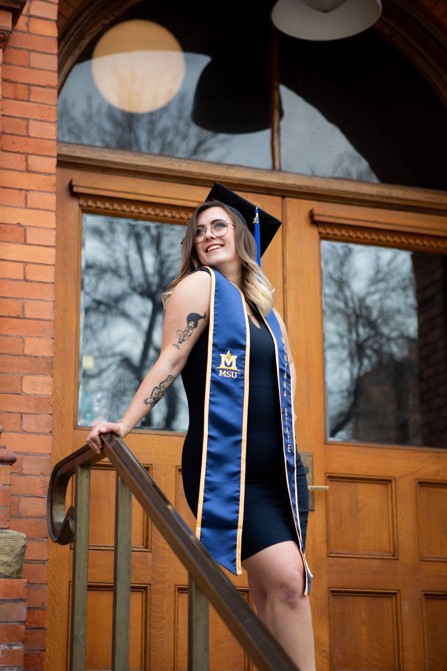 A Montana State grad stands on the steps on Montana Hall in Bozeman, Montana.