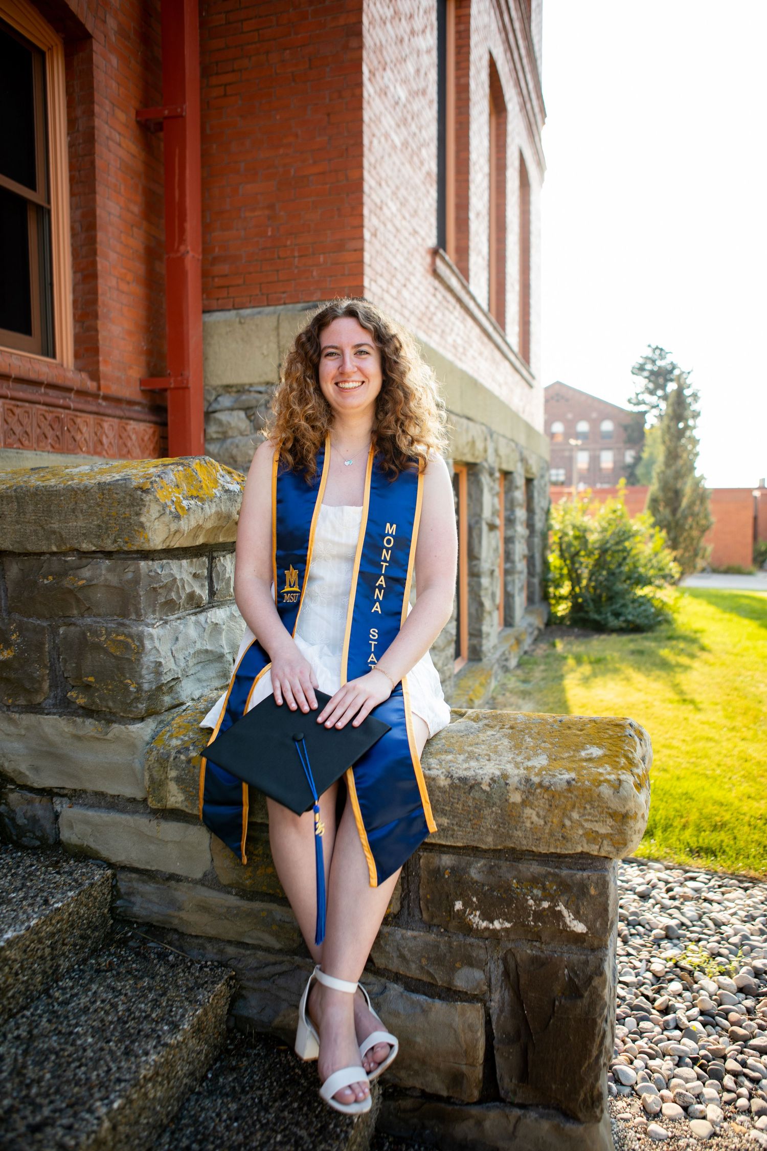 A Montana State Grad sits on the edge of Montana Hall on campus in Bozeman.