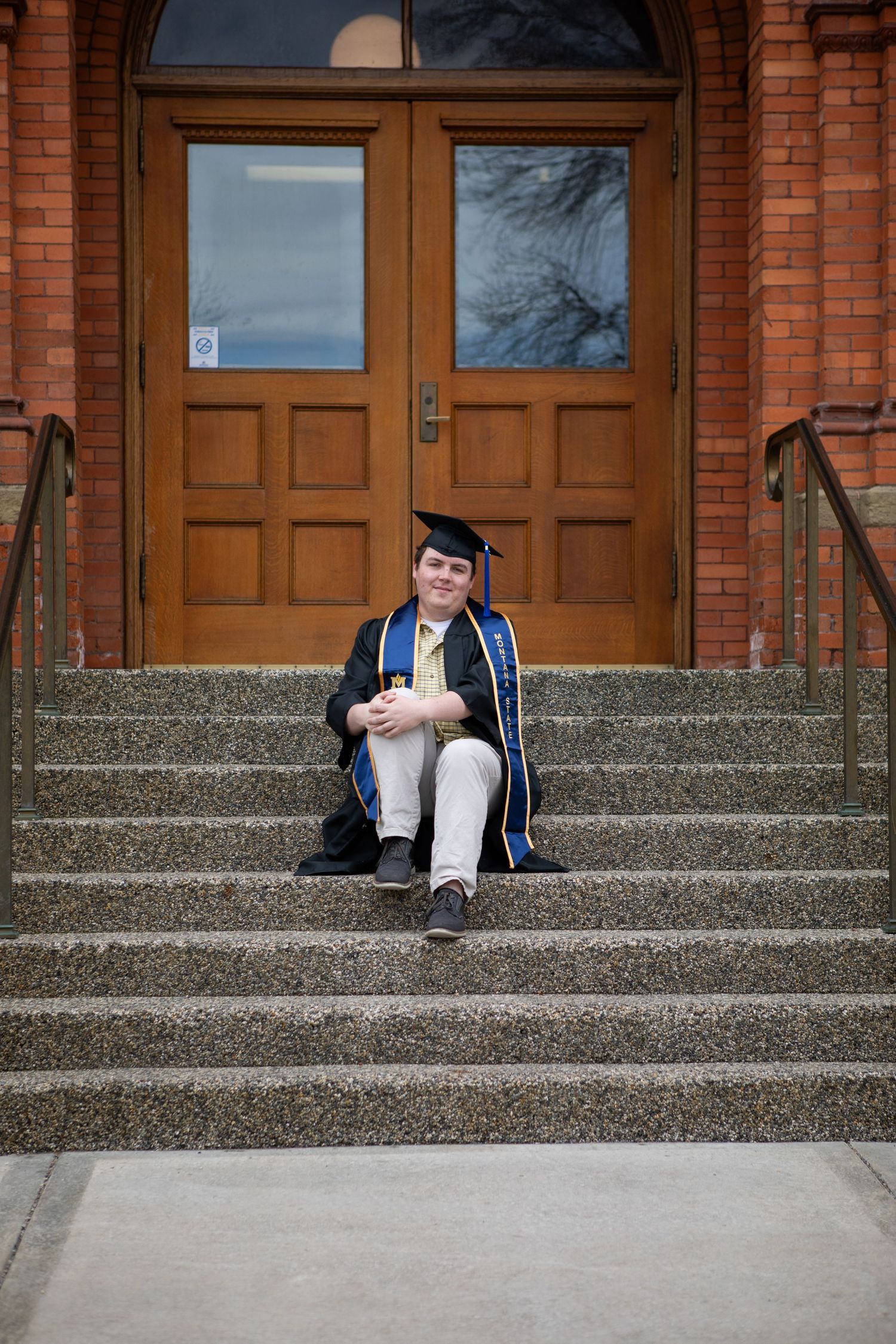 A Montana State University Grad sitting on the steps of Montana Hall.
