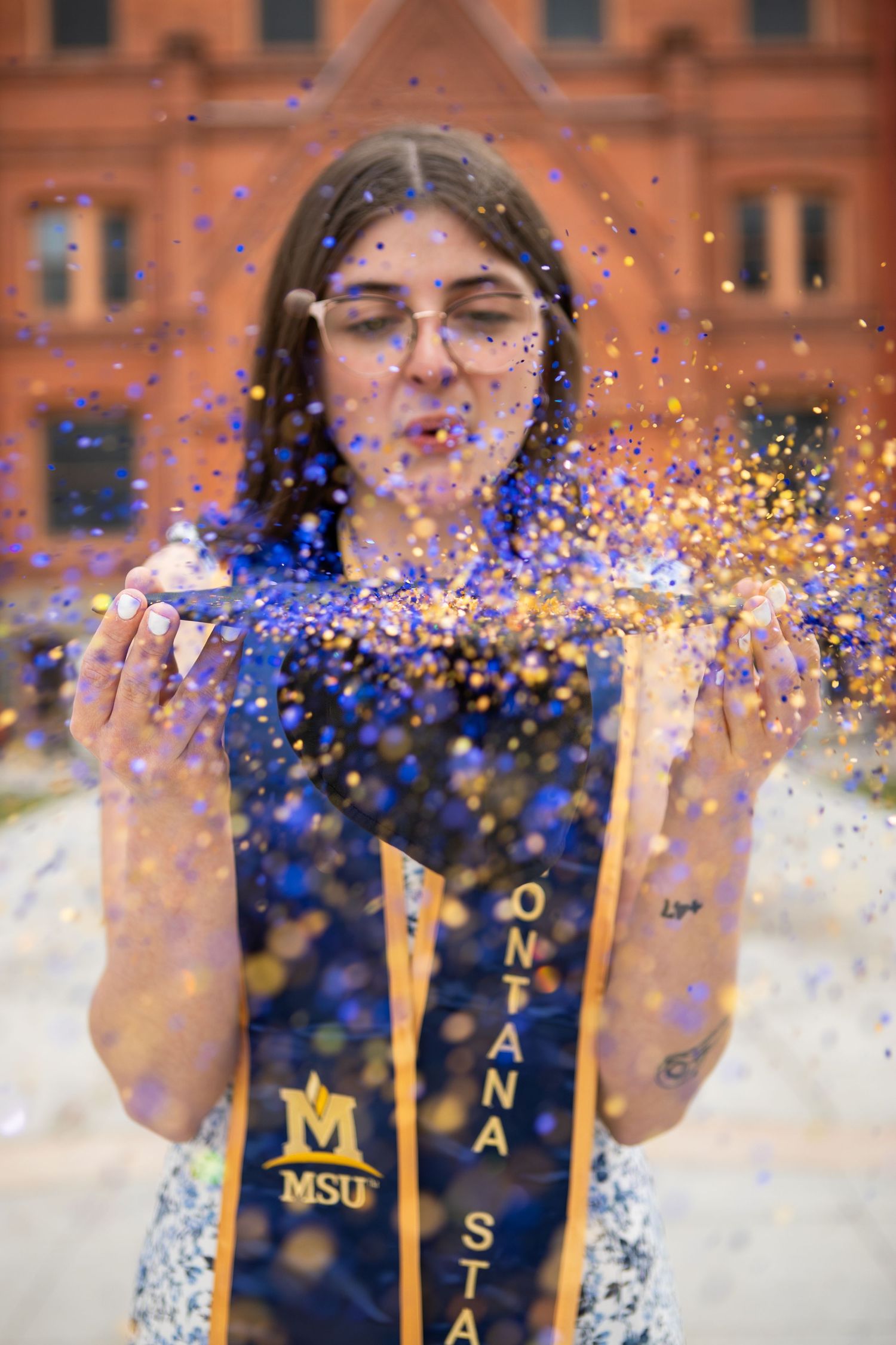 A Montana State University Grad blowing blue and gold glitter off of her cap.