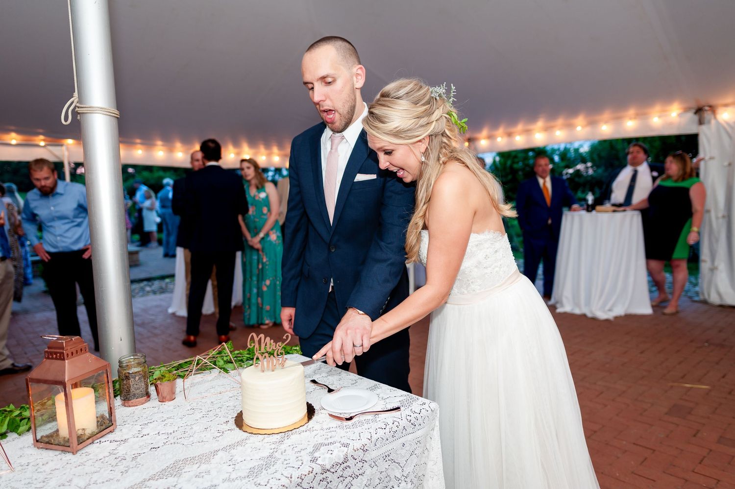 Newlyweds cutting their wedding cake together under reception tent.