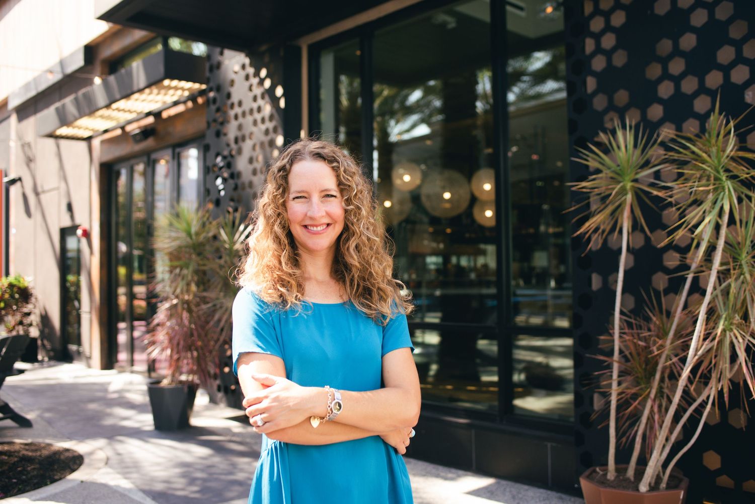 Professional headshot of someone in a bright blue top smiling in front of a modern storefront.