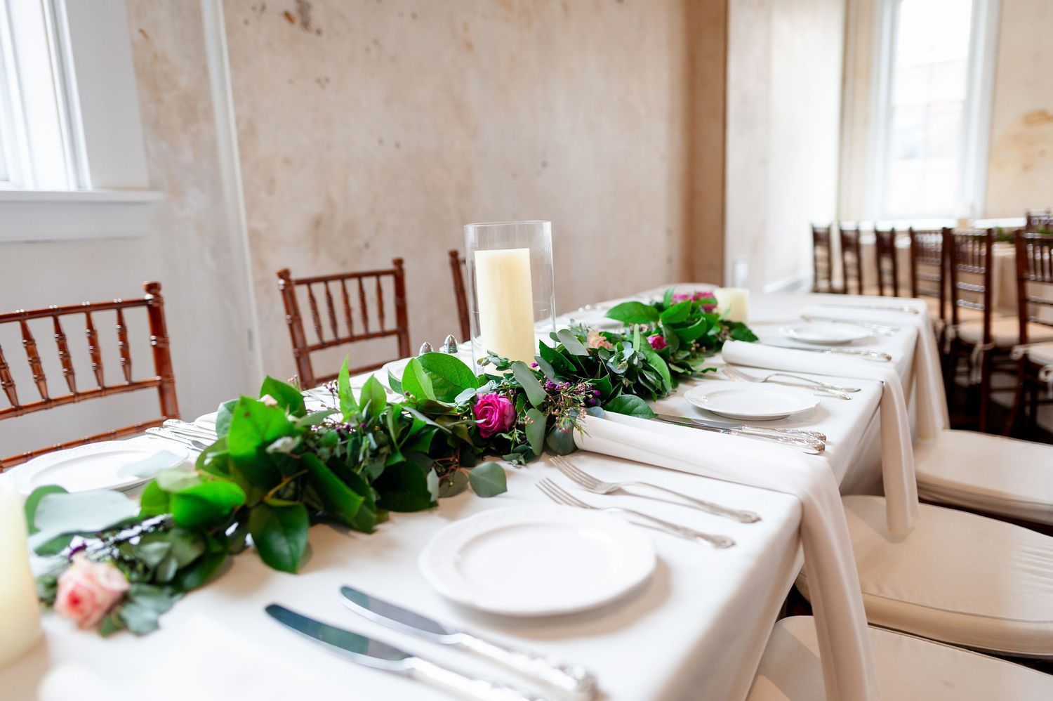 Wedding table setting with greenery garland runner and white place settings.