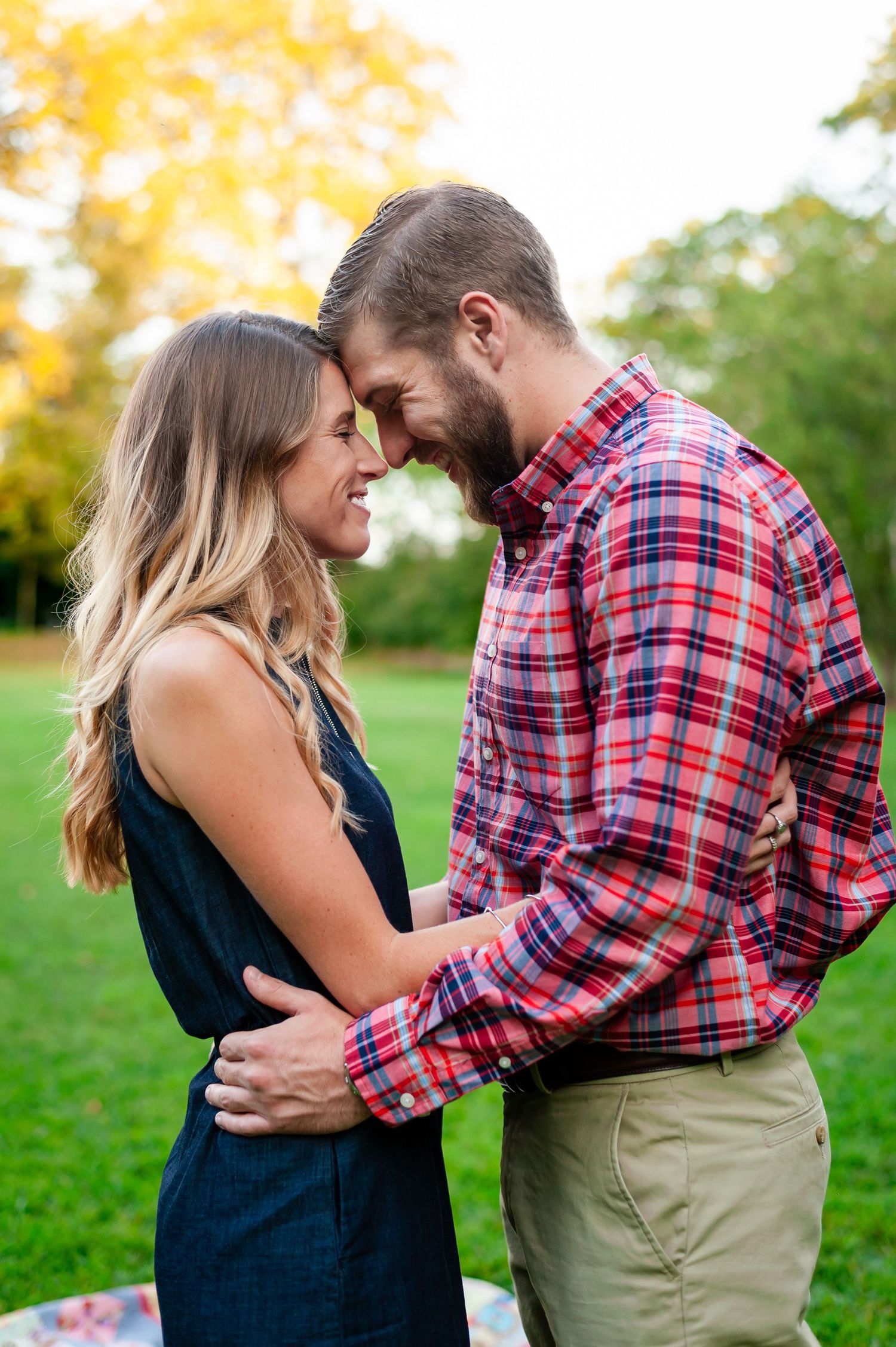 Romantic couple in casual attire embracing on autumn grass during outdoor photo session.