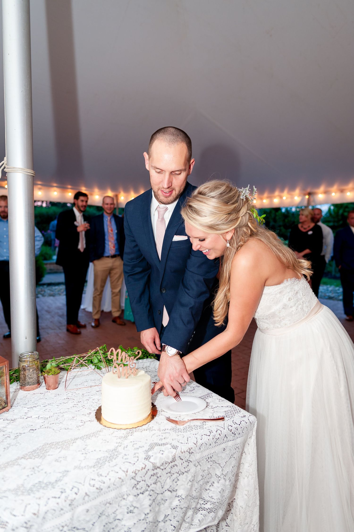 A couple in wedding attire cutting their white wedding cake together at an outdoor reception.