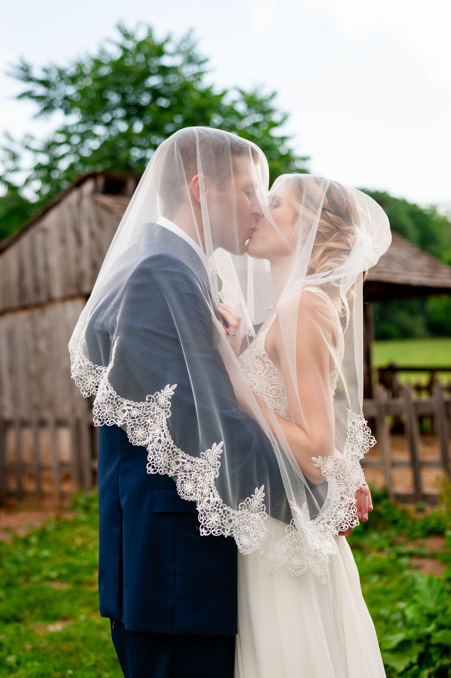 Romantic moment under delicate lace veil with rustic farm backdrop.