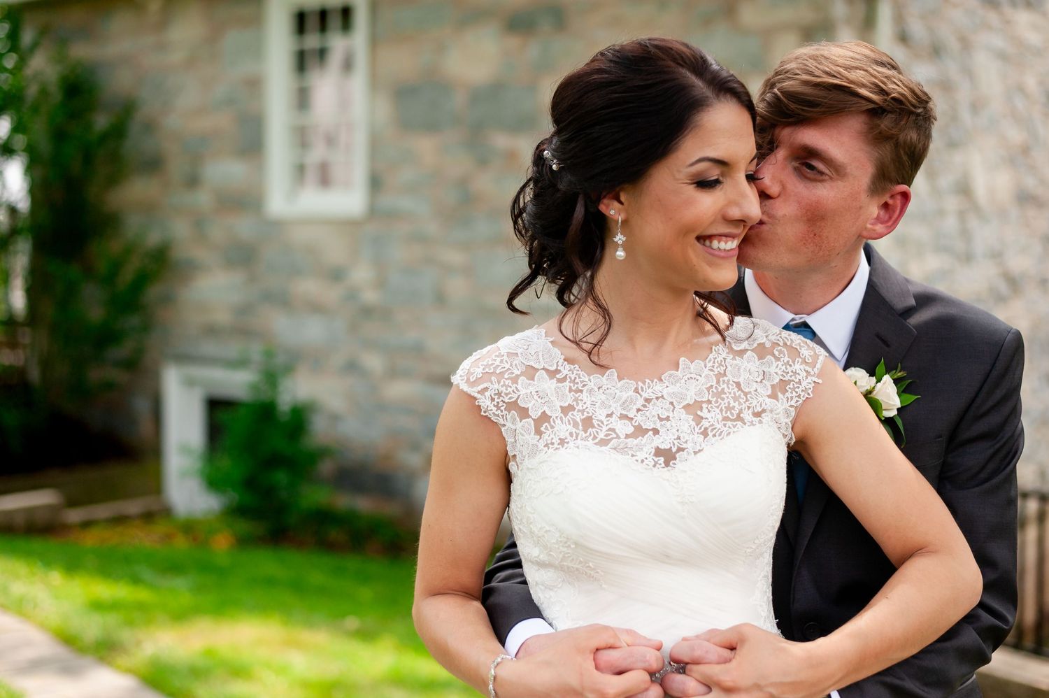 Romantic wedding moment captured in front of rustic stone wall and garden.