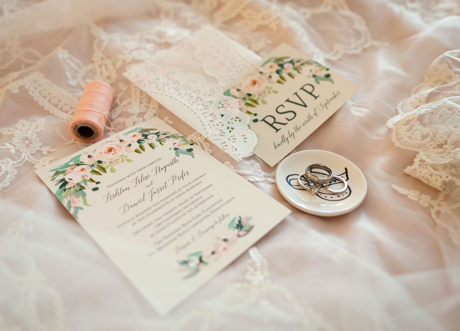 Wedding invitation with floral design and rings displayed on lace fabric.
